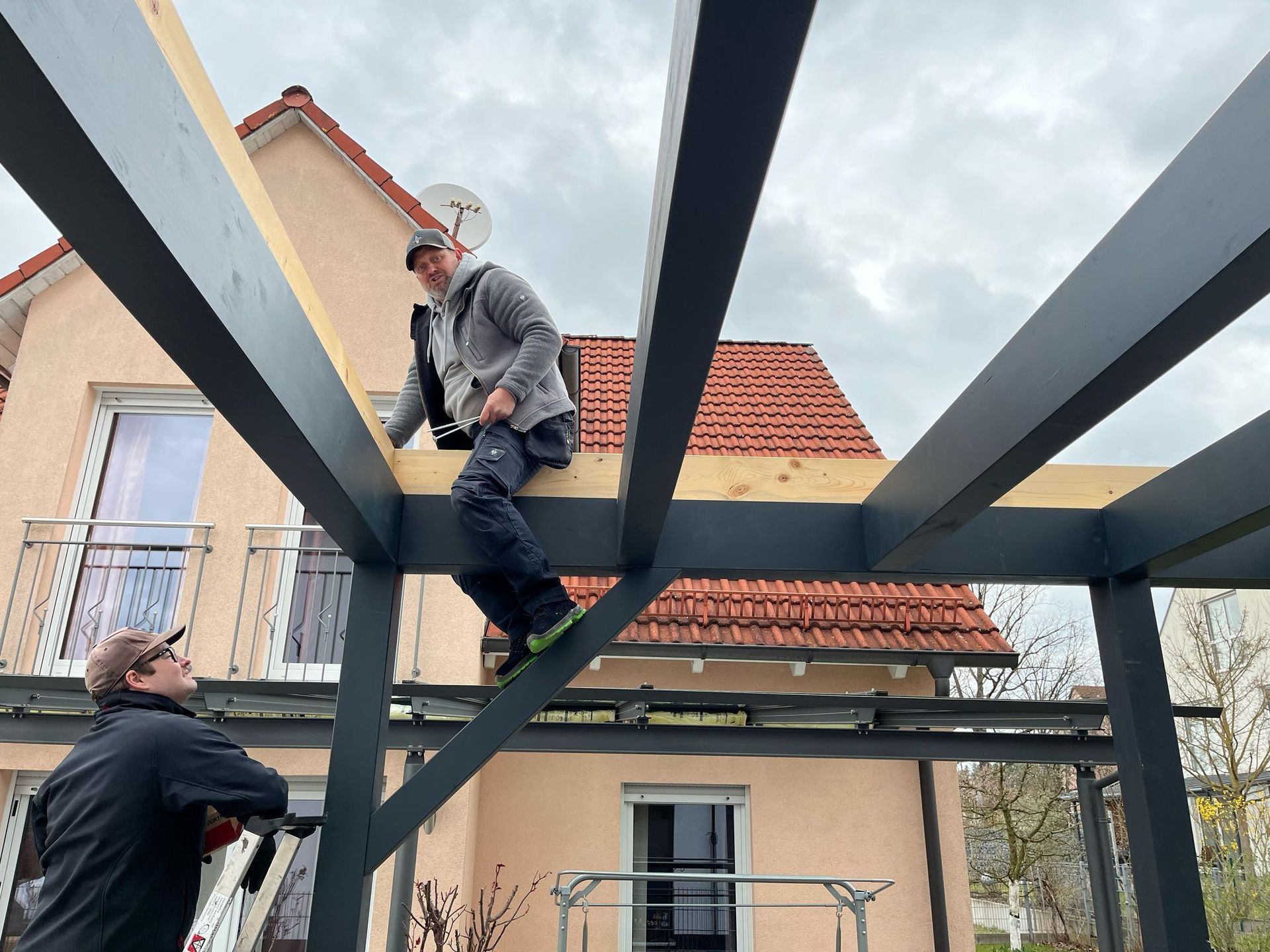 Handwerker montieren die Holzbalken eines neuen Carports an einem Wohnhaus
