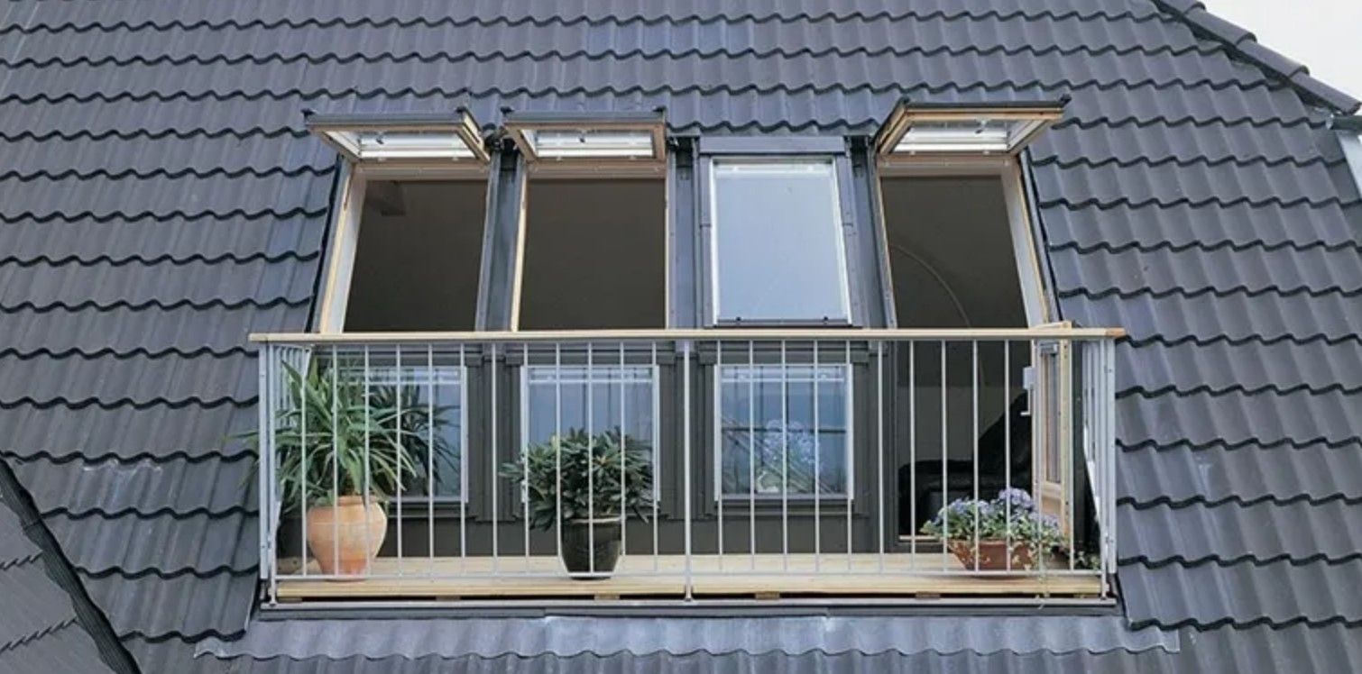 Moderner Dachbalkon mit bodentiefen Fenstern, grauem Ziegeldach und bepflanztem Balkongeländer