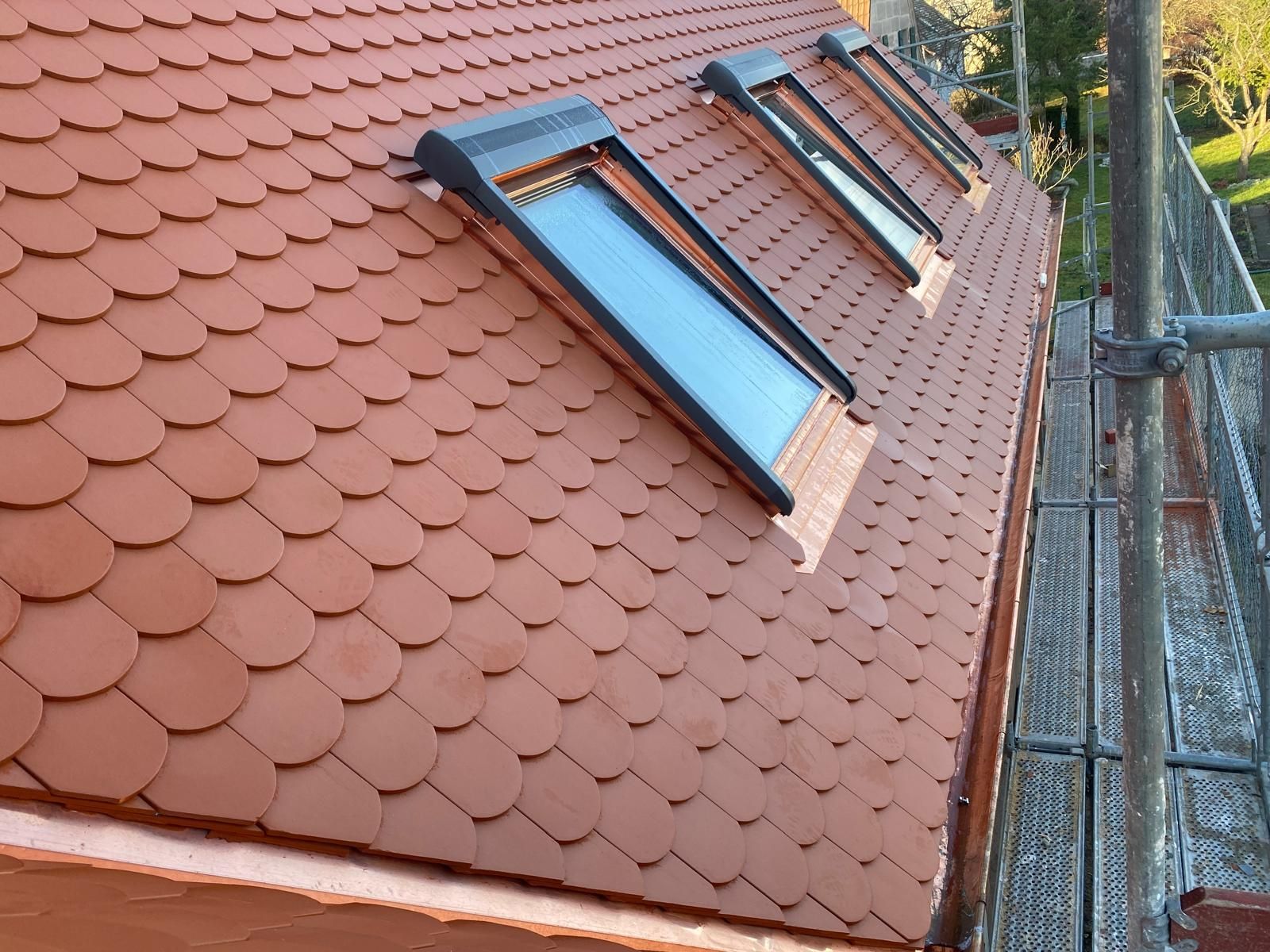 Mehrere moderne Dachfenster in einem roten Ziegeldach während Renovierungsarbeiten mit Gerüst an der Hausseite