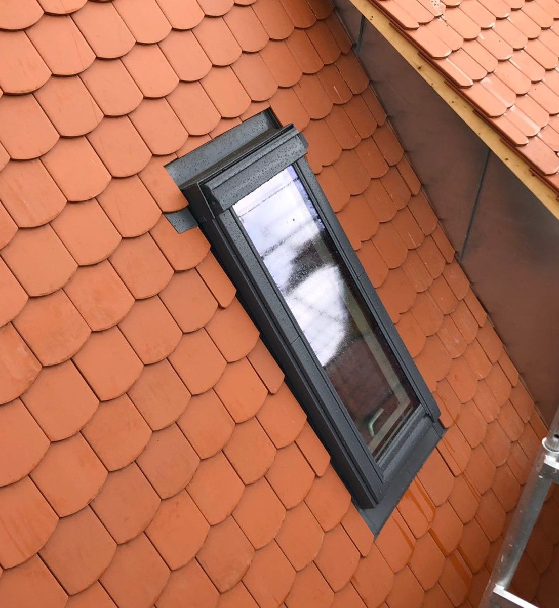 Nahaufnahme eines eingebauten Dachfensters in einem roten Ziegeldach mit sauber eingefasster Dachabdichtung.