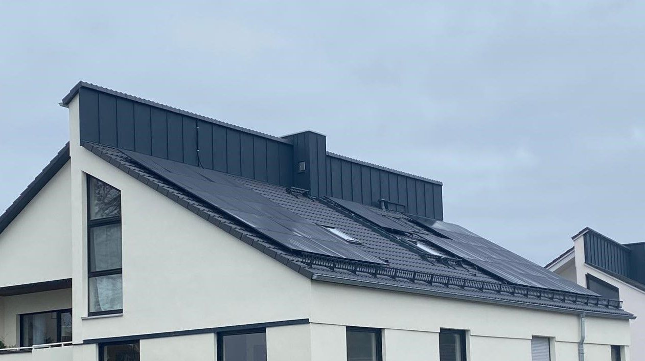 Modernes Wohnhaus mit dunkel gedecktem Satteldach und installierten Dachleitern unter bewölktem Himmel