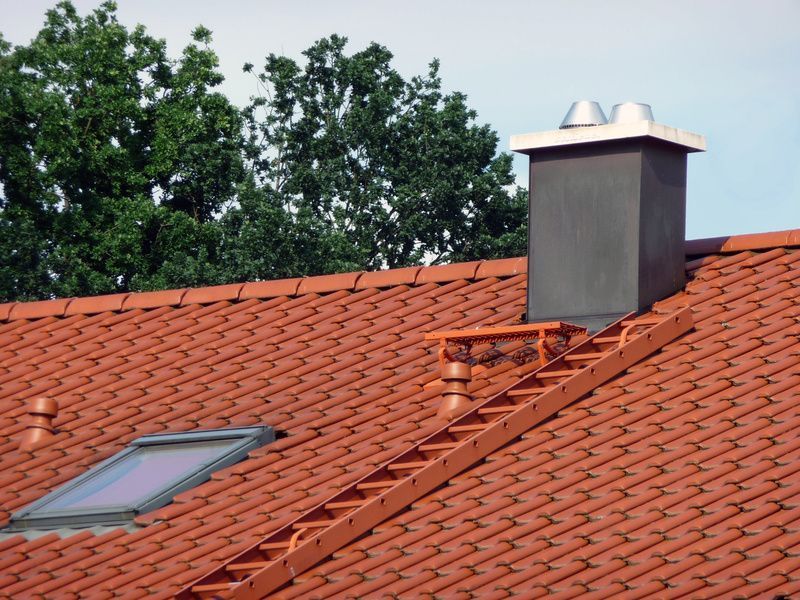 Rotes Ziegeldach mit Schornstein, Dachleiter und Sicherheitszubehör auf einem Wohngebäude.