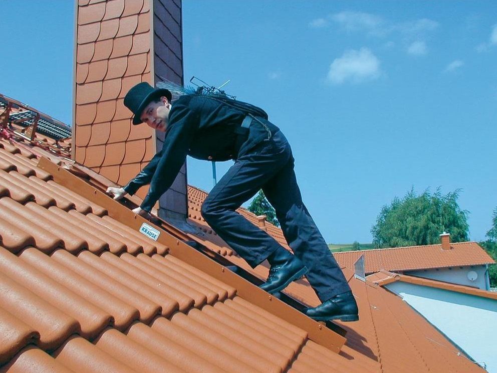 Dachdecker bei Arbeiten auf einem Ziegeldach mit Dachleiter und Schornstein.