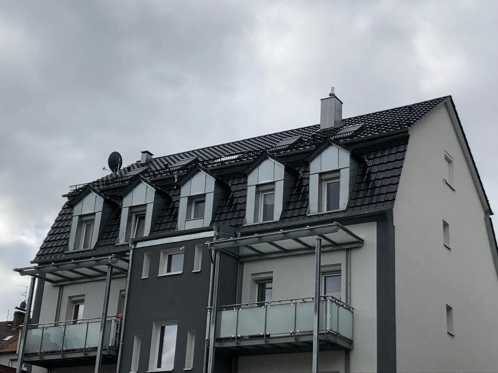 Mehrfamilienhaus mit mehreren Dachgauben und dunklem Schieferdach unter grauem Himmel