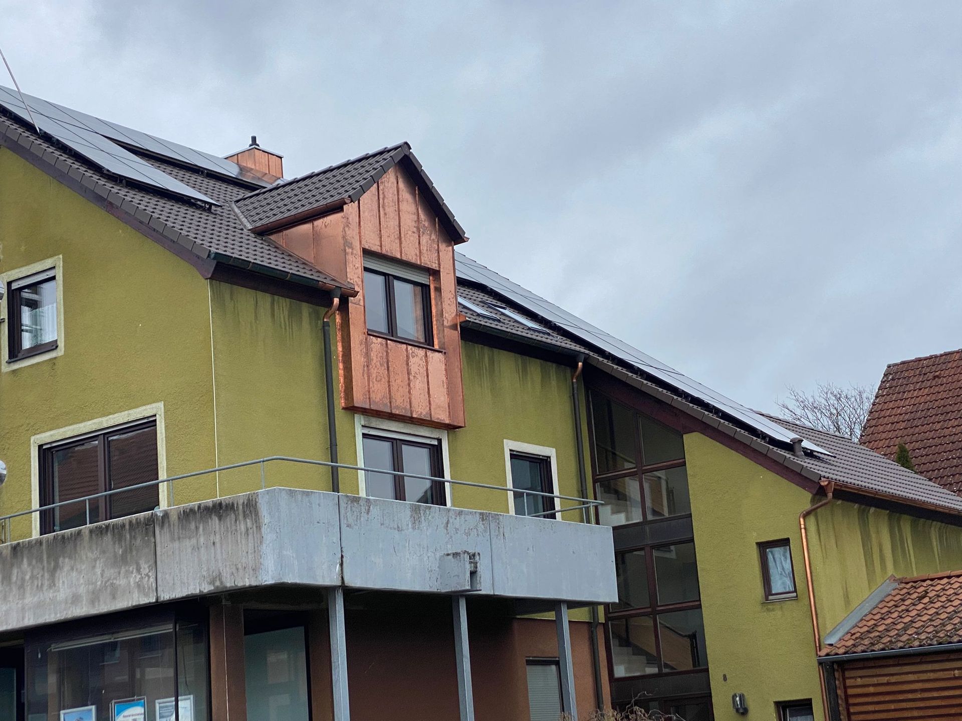 Wohnhaus mit moderner Holzgaube und dunklem Ziegeldach unter bewölktem Himmel
