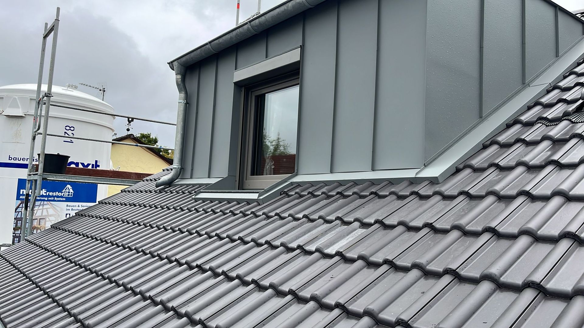 Dachgaube mit grauer Metallverkleidung auf modernem Ziegeldach bei Regenwetter