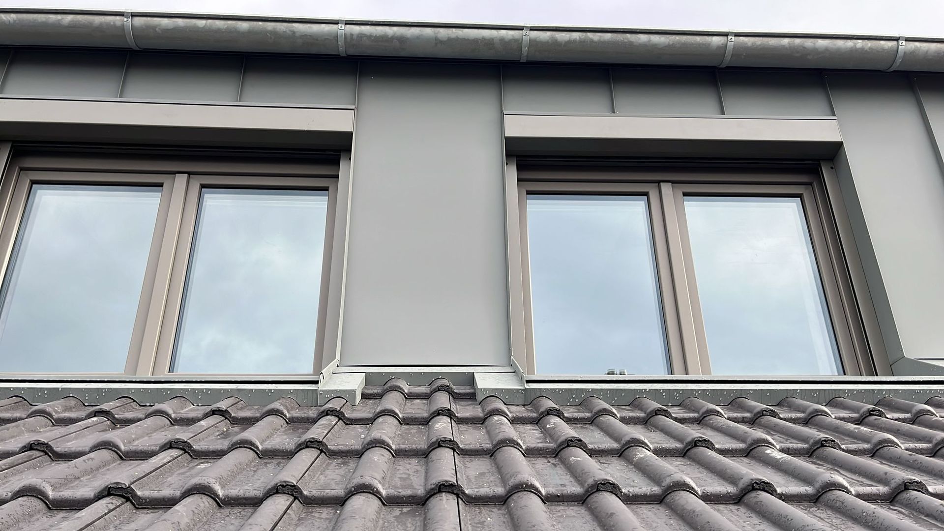 Nahaufnahme einer modern verkleideten Dachgaube mit zwei Fenstern und grauem Ziegeldach