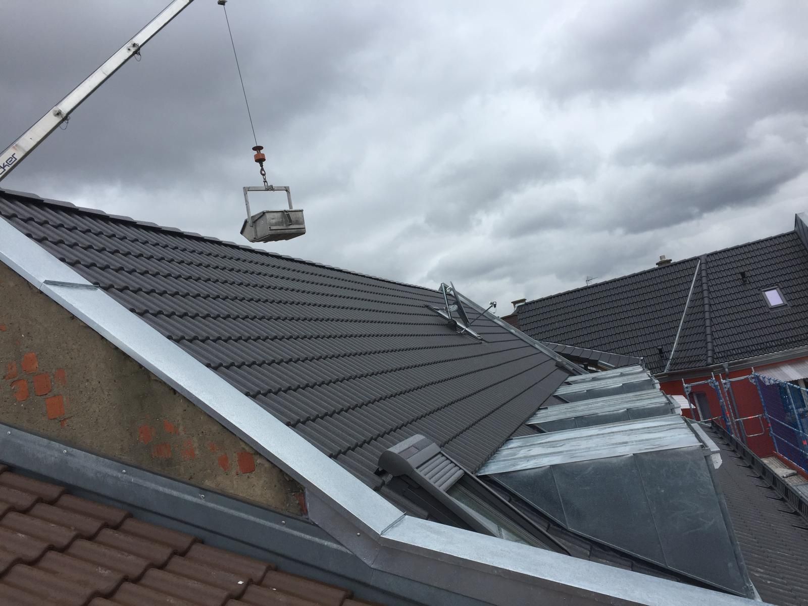 Modernes Wohnhaus mit dunkelgrauer Dacheindeckung während der Montagearbeiten mit Kran bei bewölktem Himmel