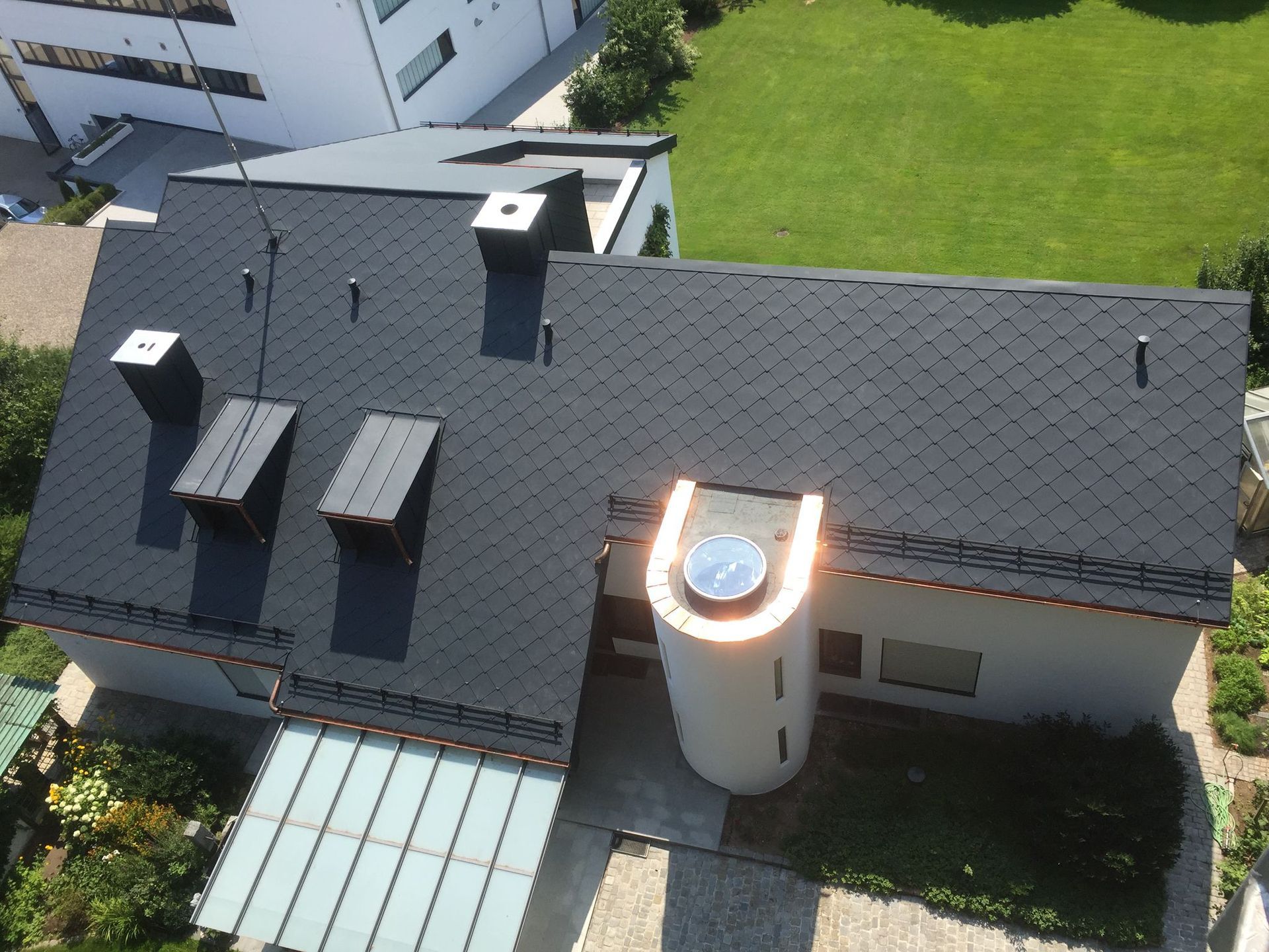 Luftaufnahme eines Wohnhauses mit dunkler Dacheindeckung, mehreren Dachfenstern und modernem Schornstein