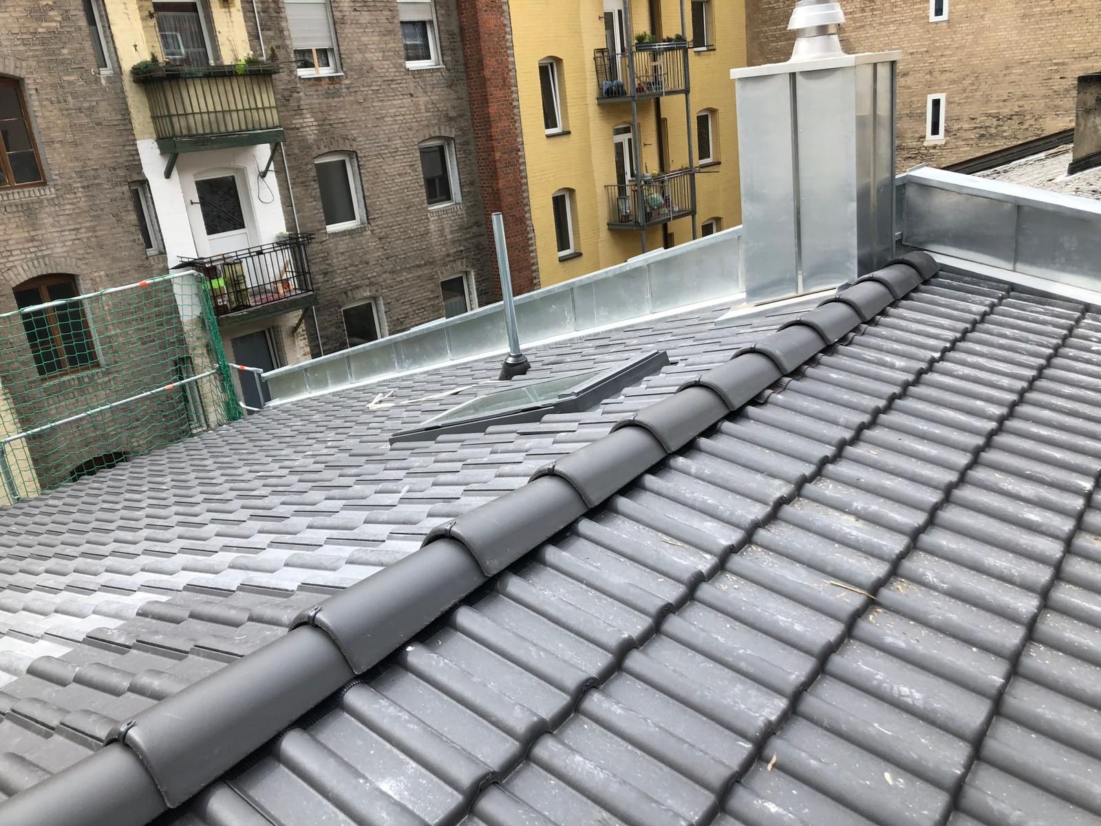 Modern saniertes Steildach mit dunkelgrauen Dachziegeln und präzise verarbeitetem Firstbereich in urbaner Umgebung