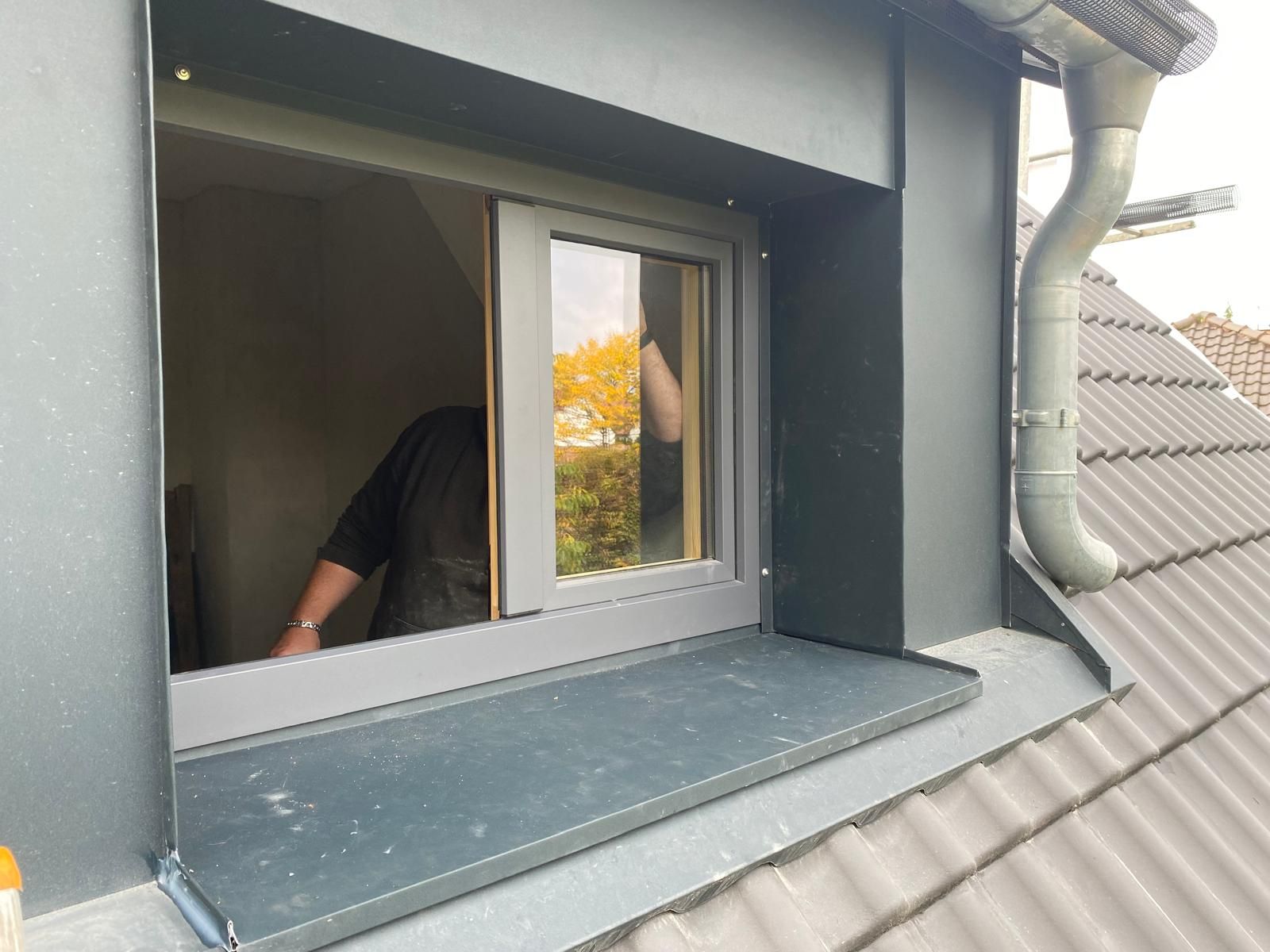 Neu eingebautes Dachfenster mit anthrazitfarbener Verkleidung und moderner Dachentwässerung an einem Wohnhaus