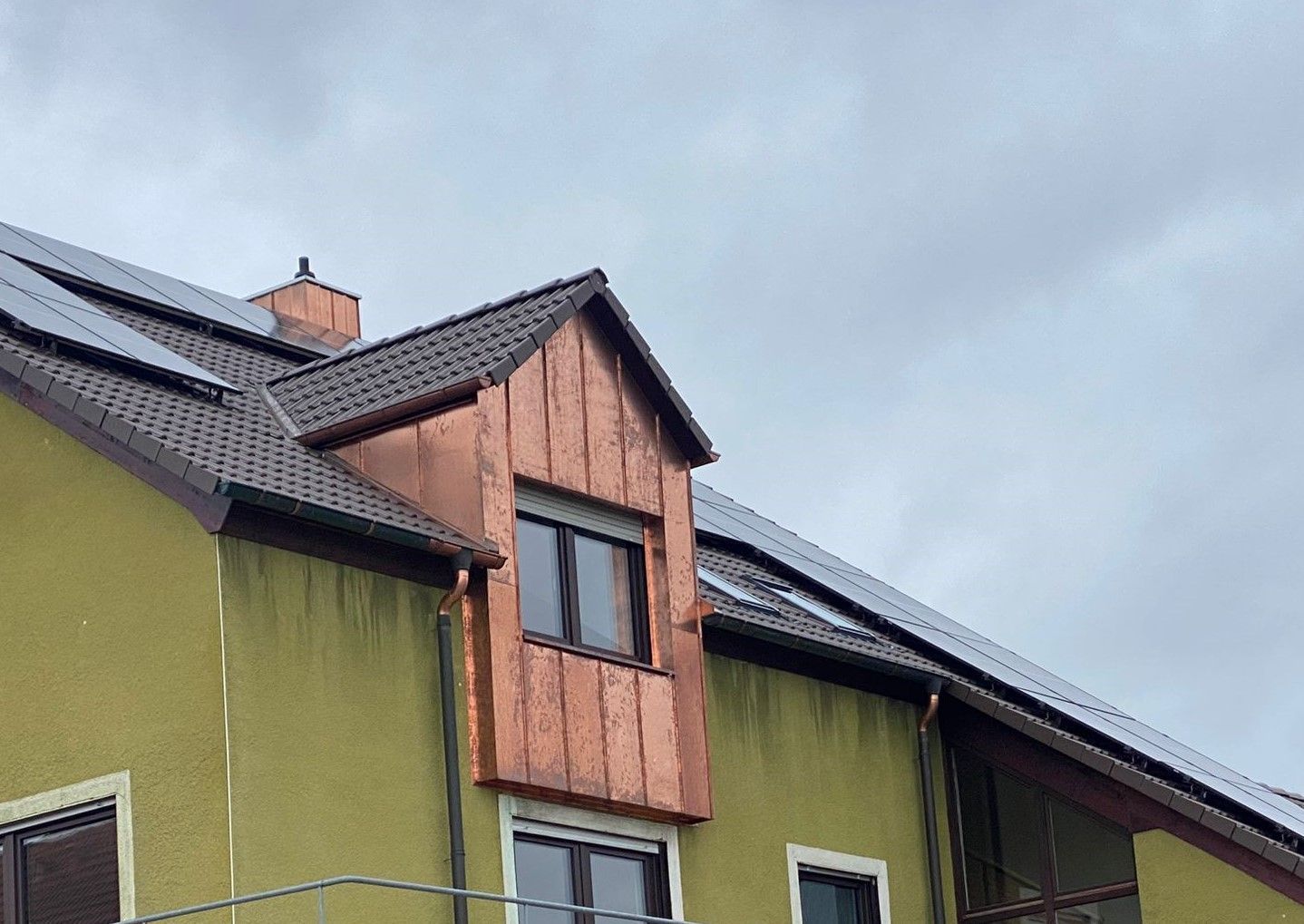 Moderne Holzgaube mit großem Fenster an einem Steildach unter grauem Himmel
