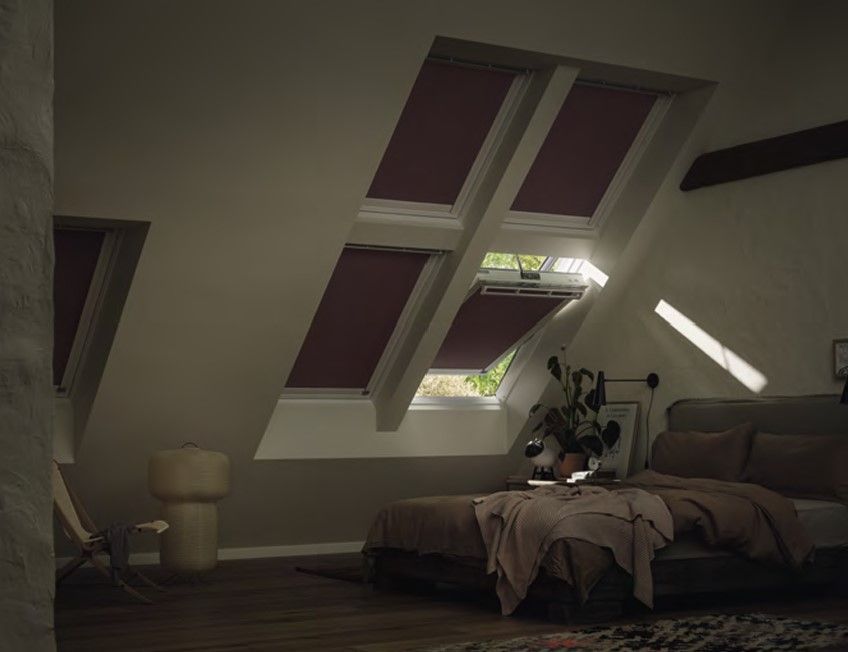 Schlafzimmer mit mehreren Dachfenstern und farbigen Verdunkelungsrollos.