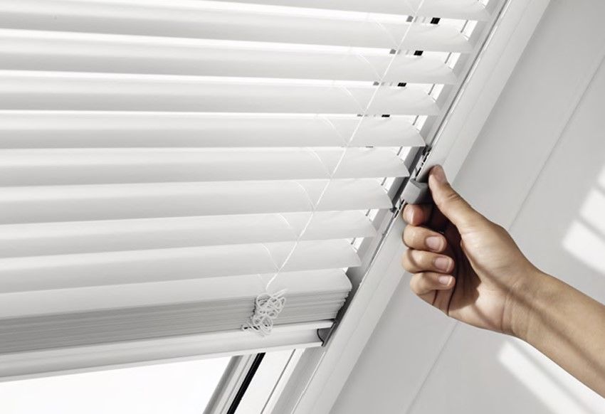 Hand bedient ein weißes Plissee-Innenrollo am Dachfenster.
