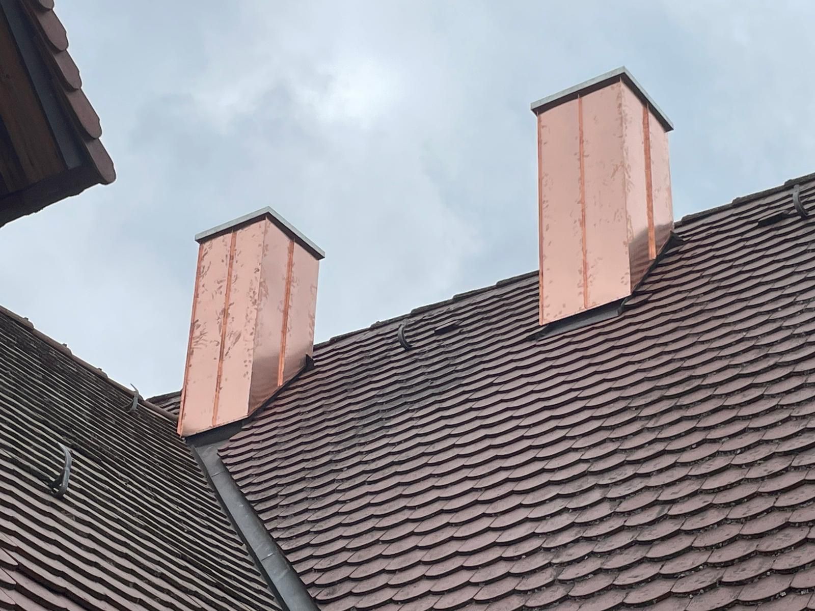 Zwei moderne Schornsteine auf einem dunklen Ziegeldach