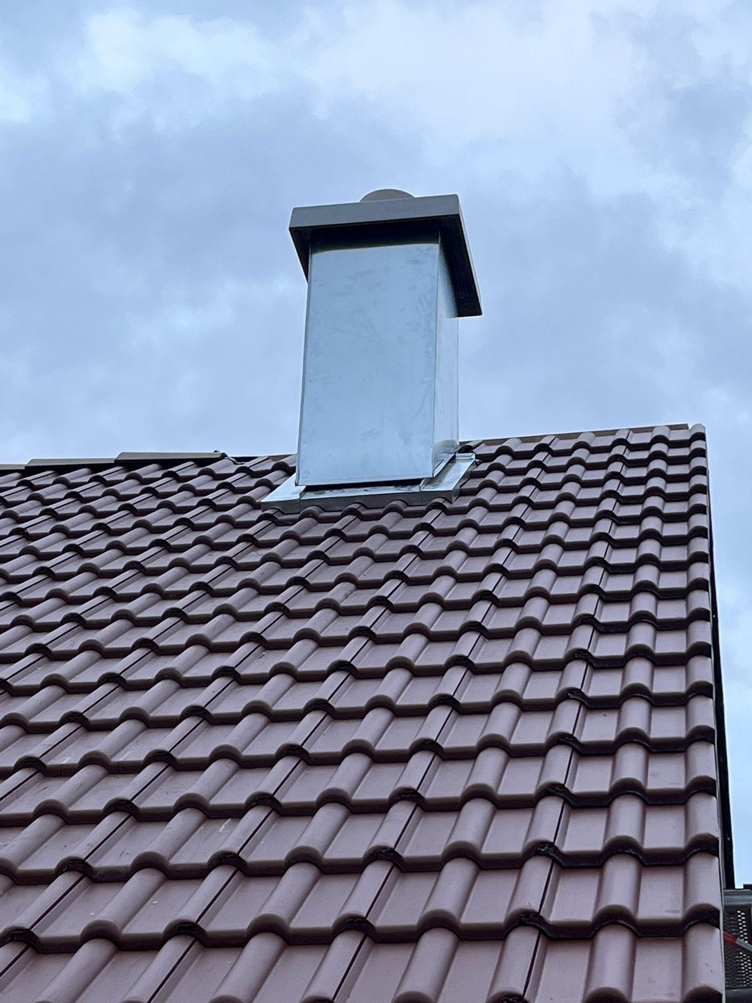 Heller Schornstein mit Abdeckung vor bewölktem Himmel
