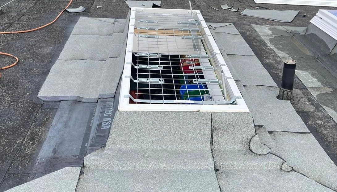 Geöffnete Lichtkuppel auf einem Flachdach mit sichtbarer Unterkonstruktion und farbigen Elementen im Inneren.