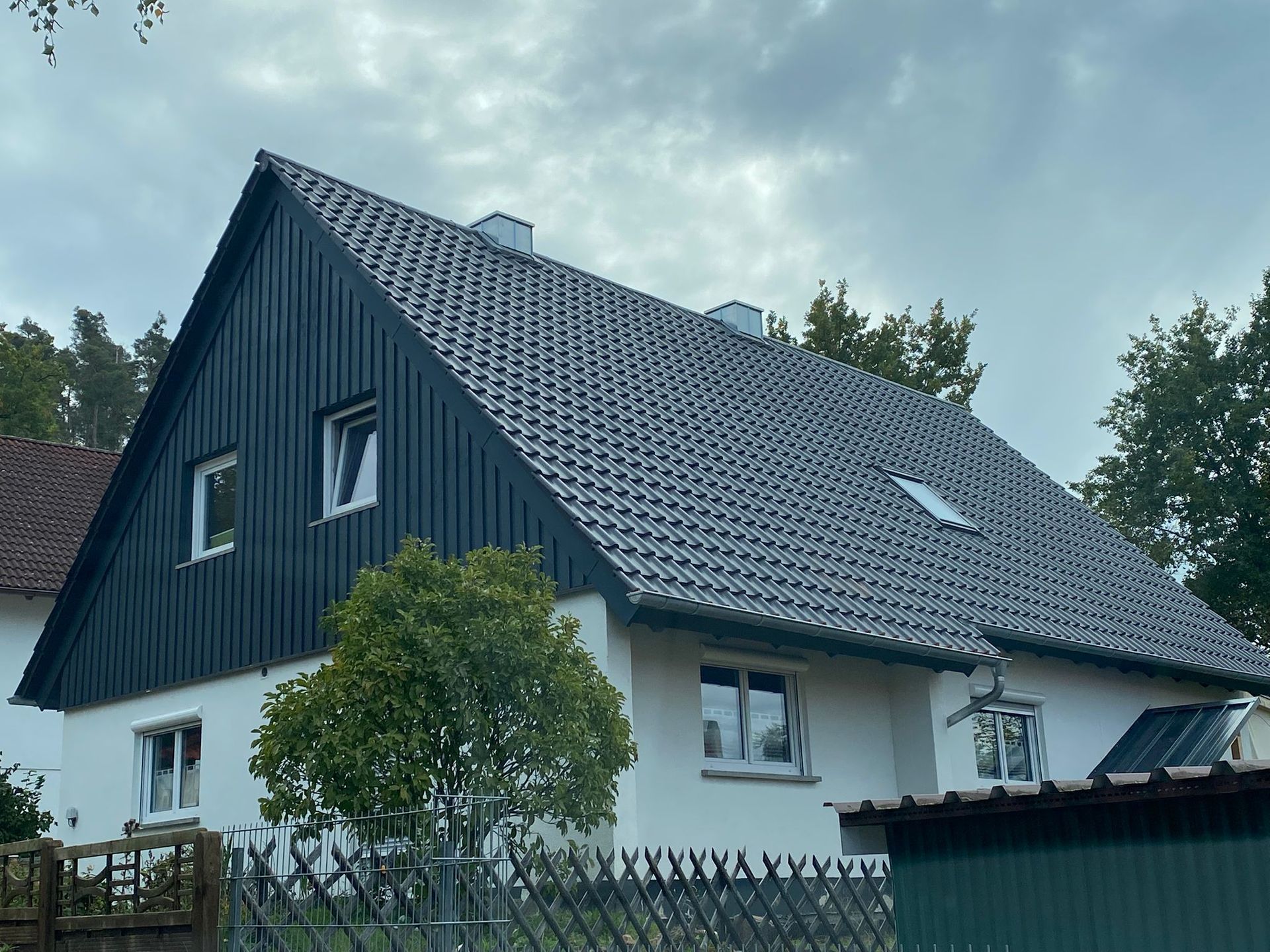 Einfamilienhaus mit dunklem Steildach und moderner Dachdeckung unter bewölktem Himmel