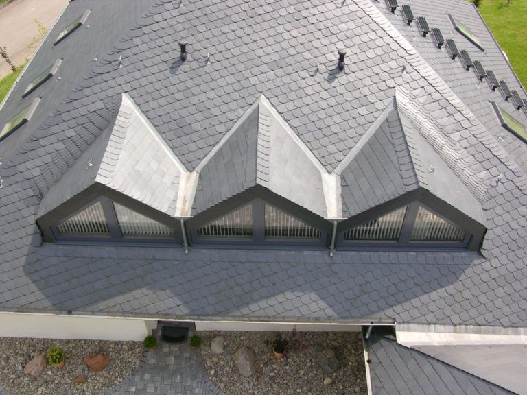 Steildach mit mehreren Gauben und grauer Schindeldeckung aus der Vogelperspektive