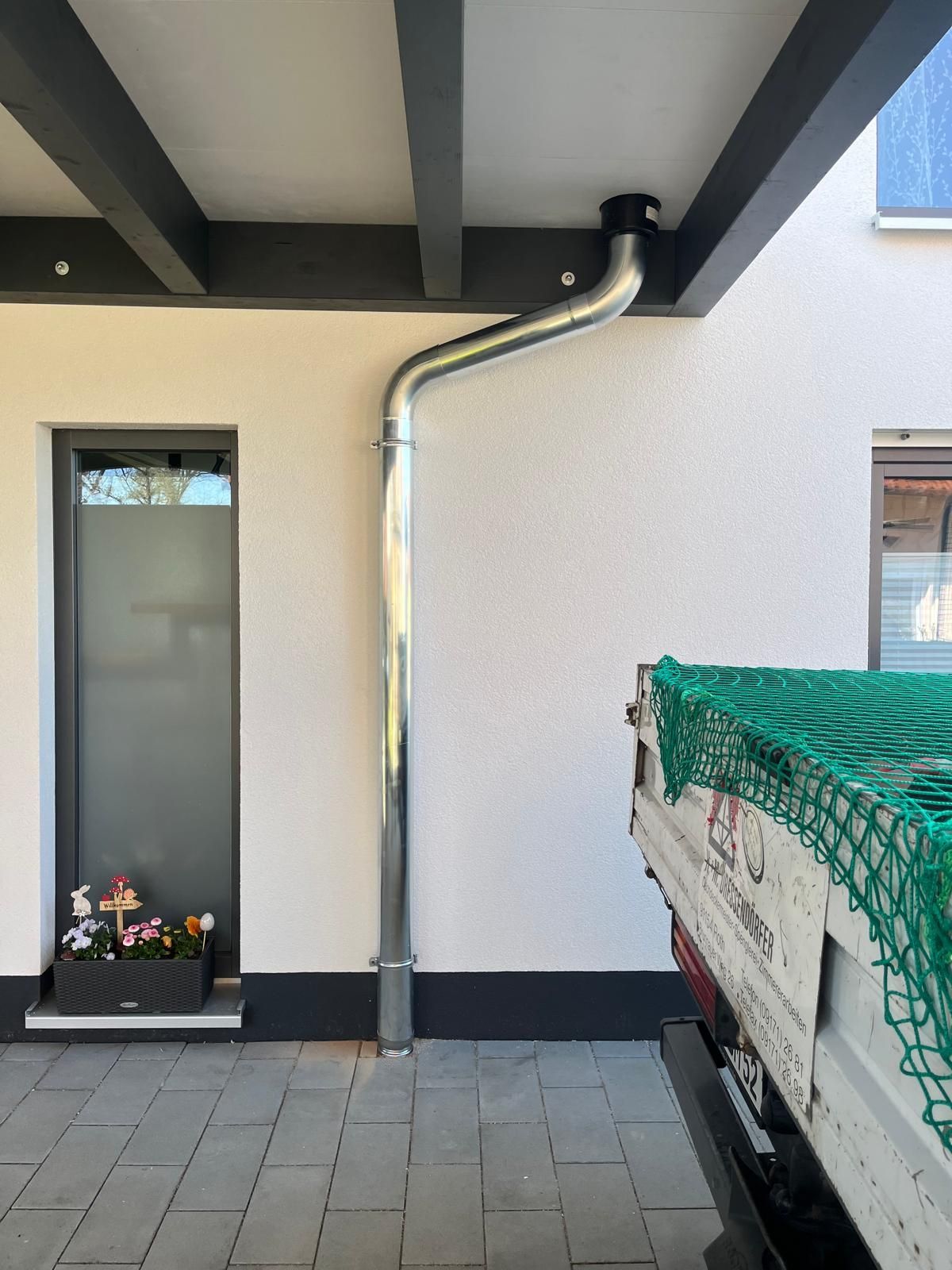 Fallrohr und Dachrinne unter einem Carport mit sichtbarer Holzbalkenkonstruktion