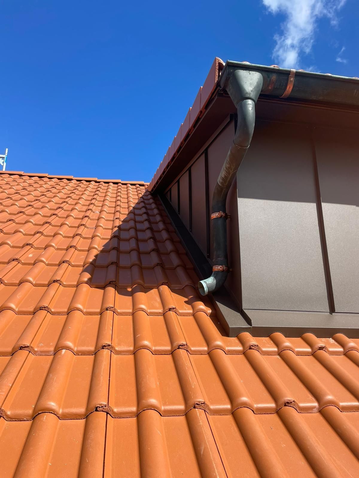 Dachrinne und Fallrohr an einem modernen Ziegeldach unter blauem Himmel