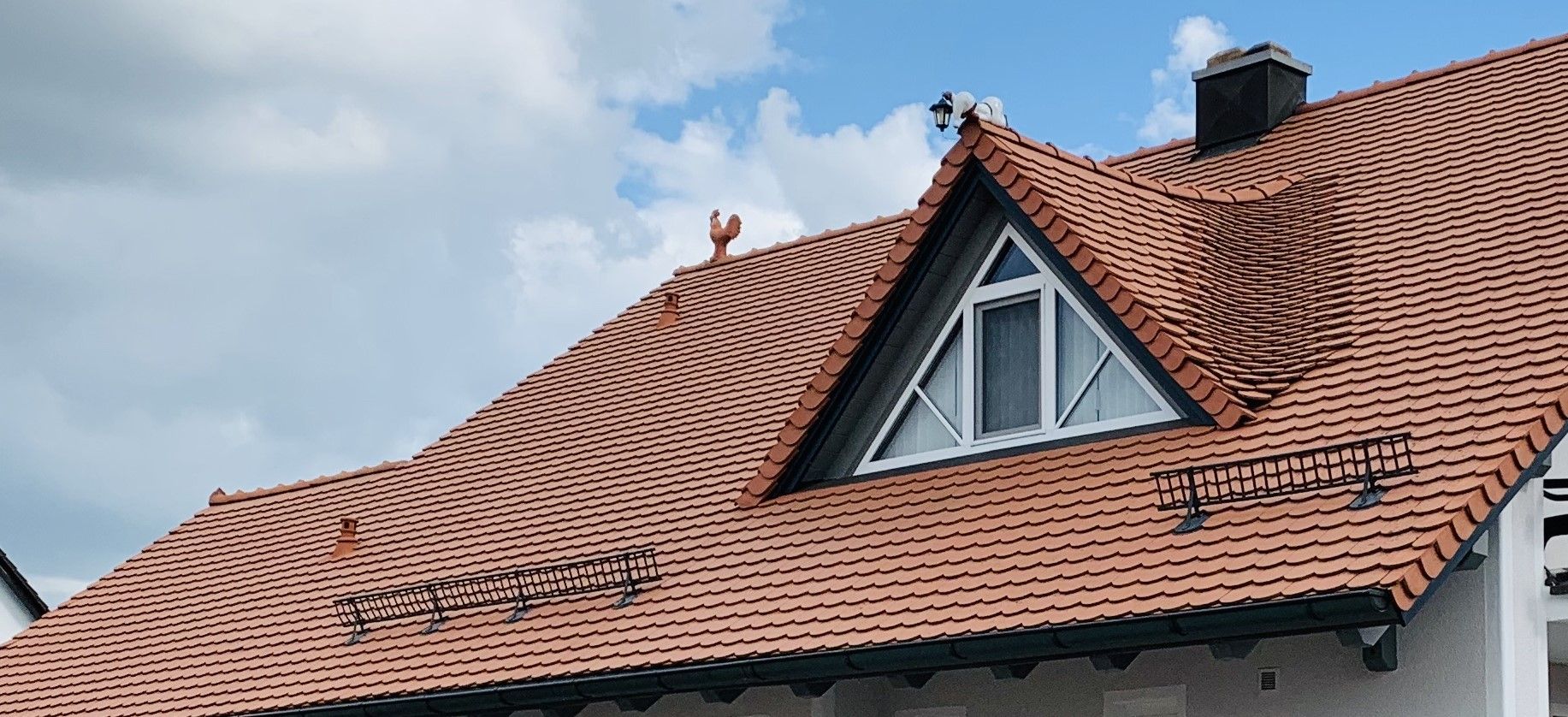 Steiles Ziegeldach mit montierten Schneefanggitter-Systemen und Dachfenster.