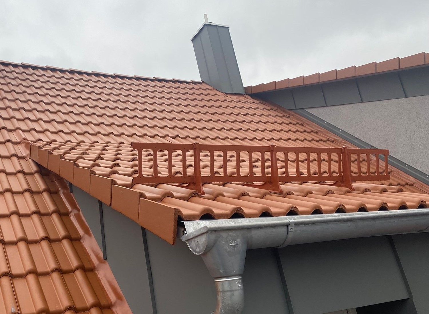 Ziegeldach mit Schneefanggitter und Dachsicherheitsanlagen auf einem Wohnhaus.