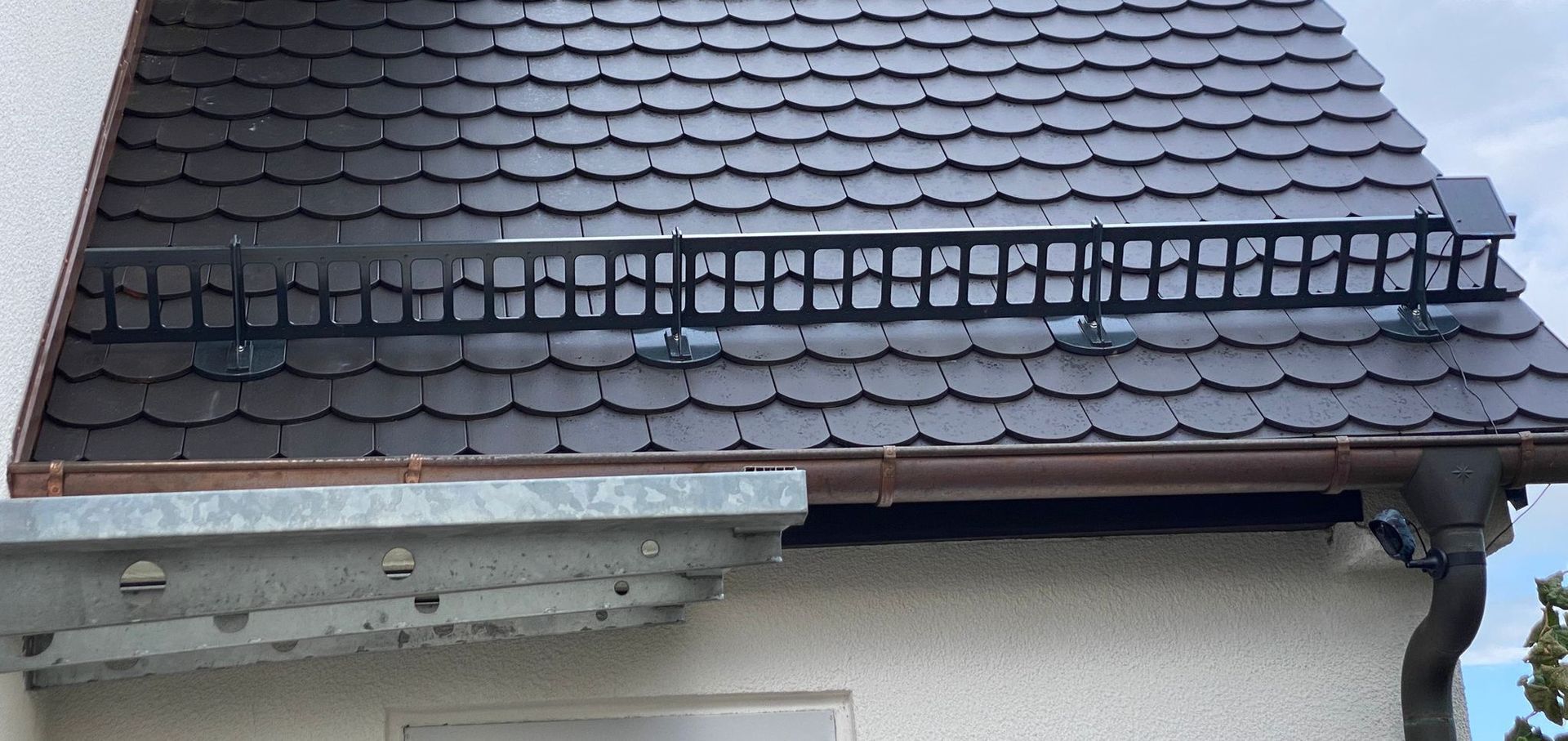 Dunkles Schieferdach mit montiertem Schneefanggitter an der Dachkante.