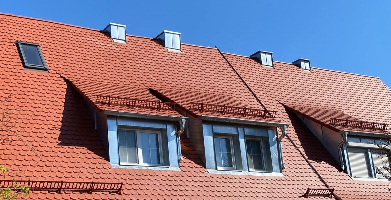 Rotes Ziegeldach mit Dachfenstern und installiertem Schneefanggitter.