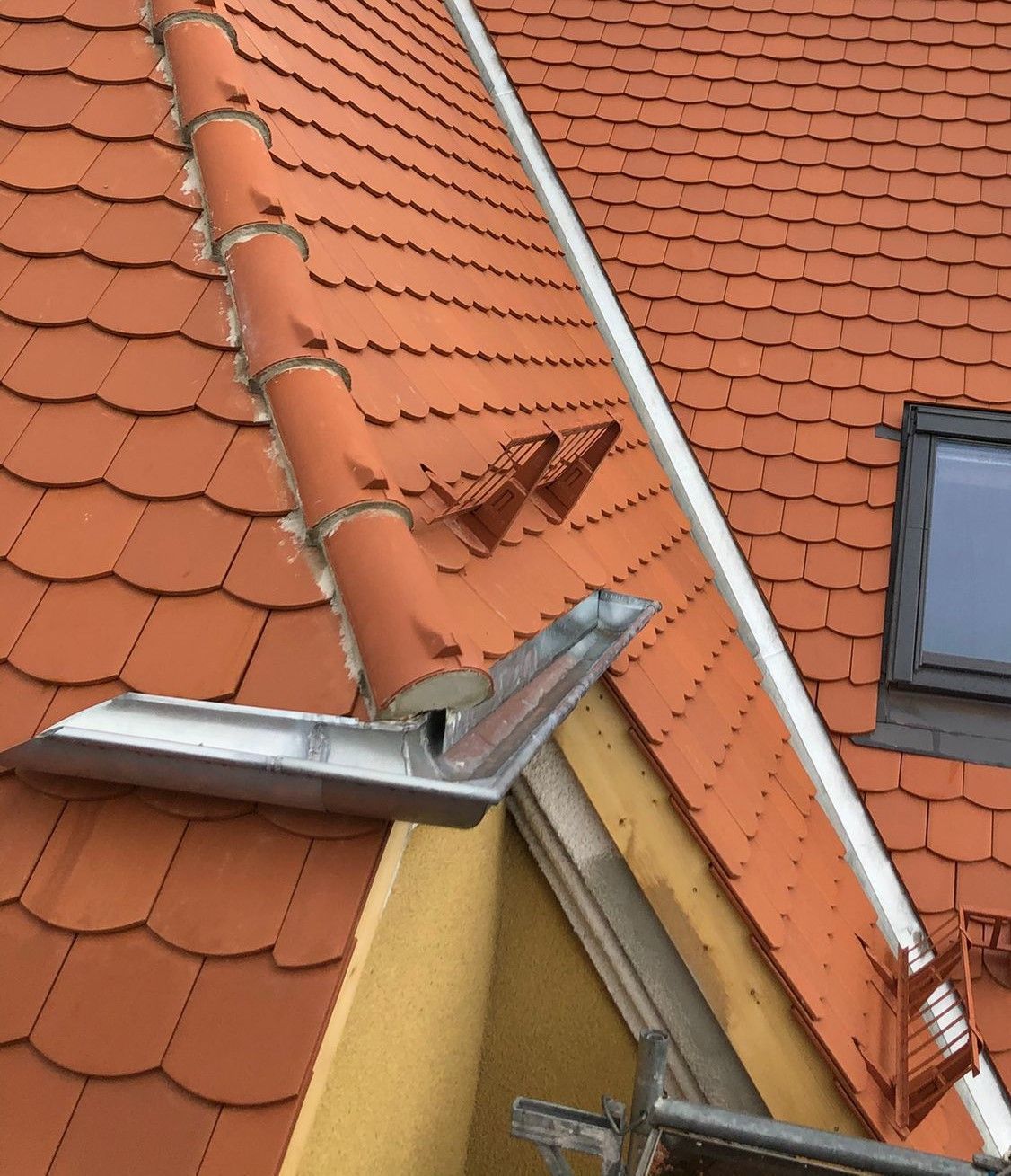 Detailansicht eines Ziegeldachs mit Schneefanghaken und Dachentwässerung.
