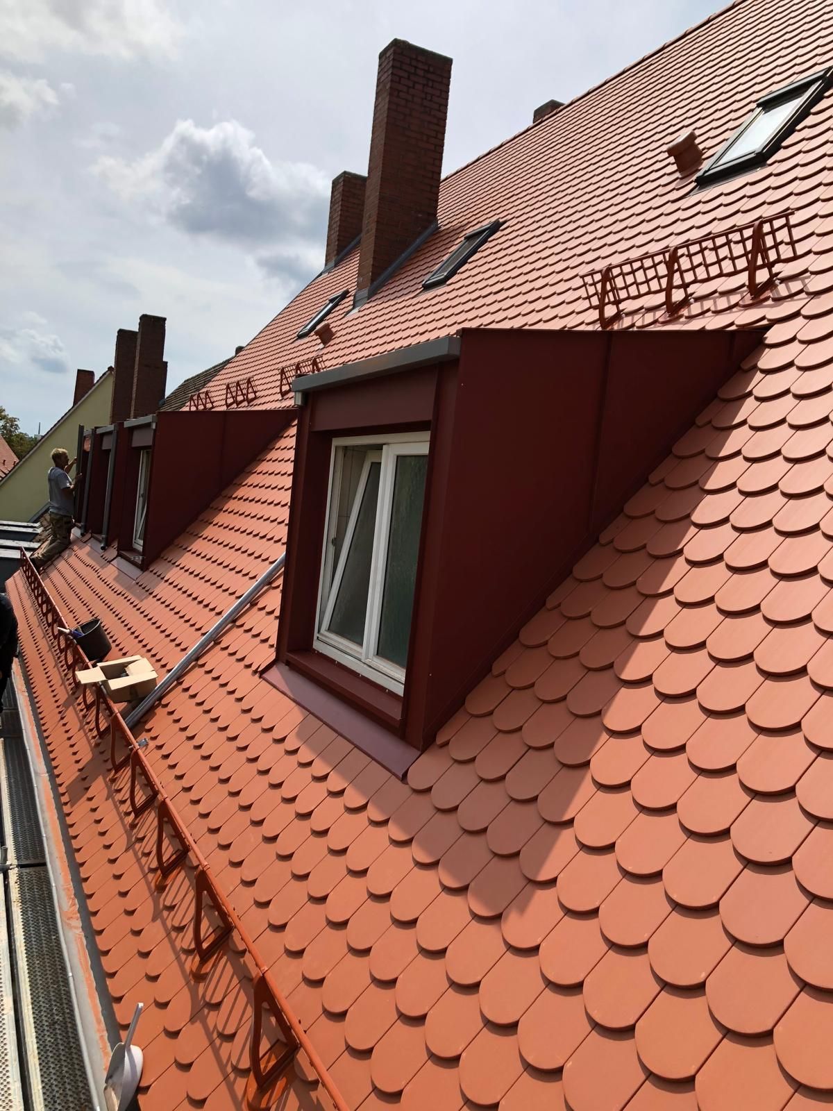 Mehrstöckiges Wohnhaus mit rotem Ziegeldach und montierten Schneefanggittern.