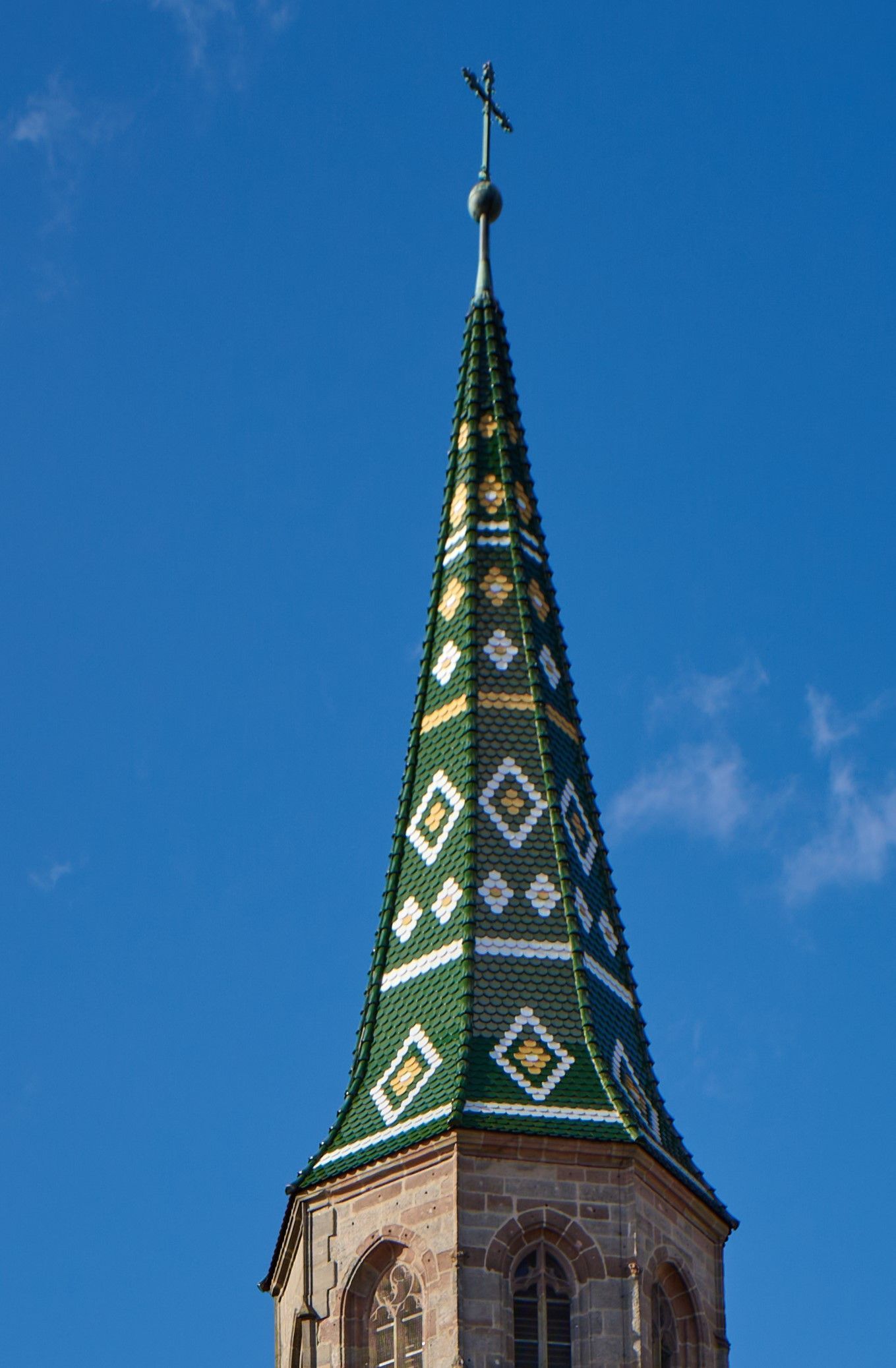 Kirchturmspitze mit Kreuz und Wetterfahne vor blauem Himmel auf einem Steildach