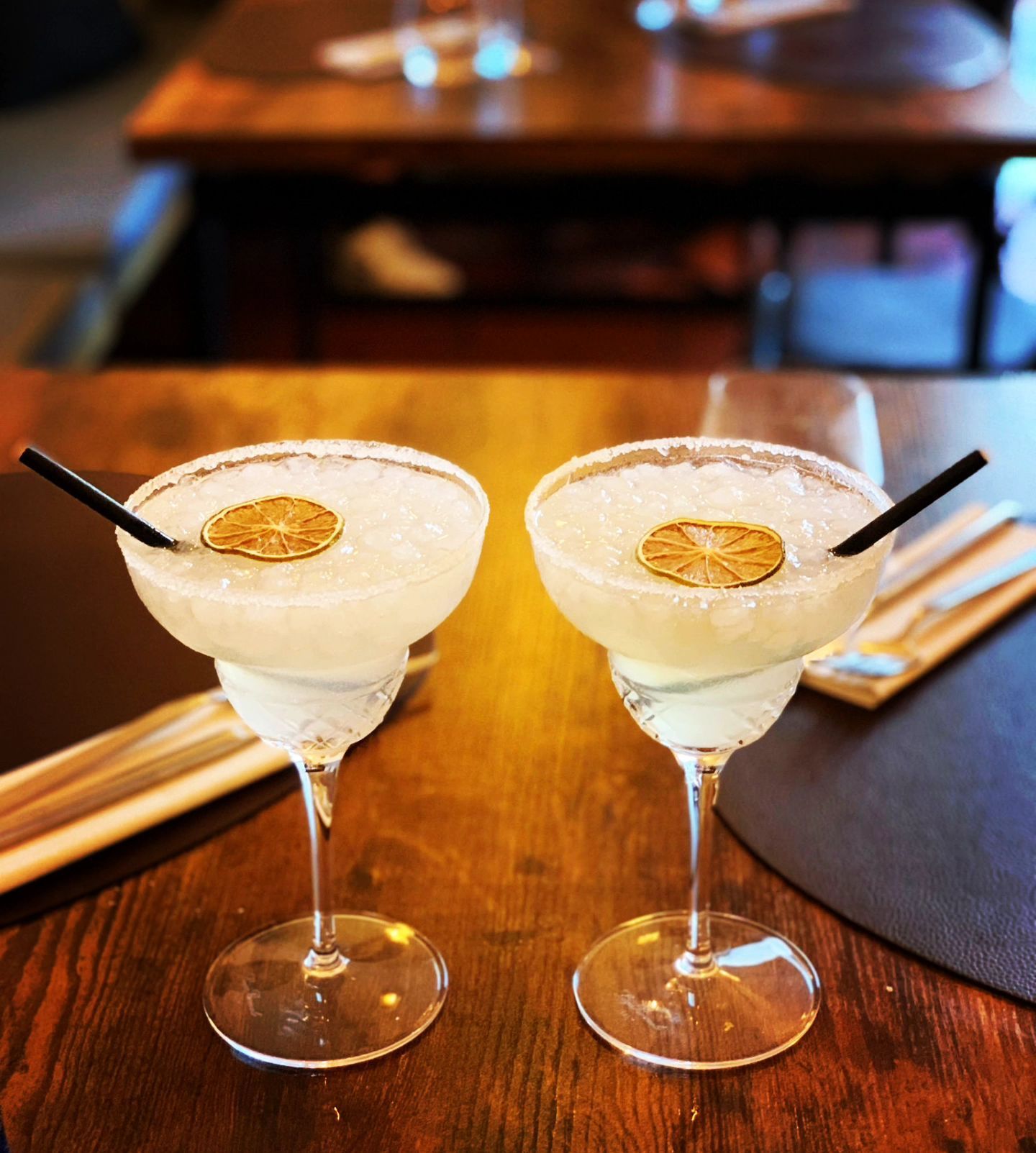 Dos copas de martini con pajitas sobre una mesa de madera
