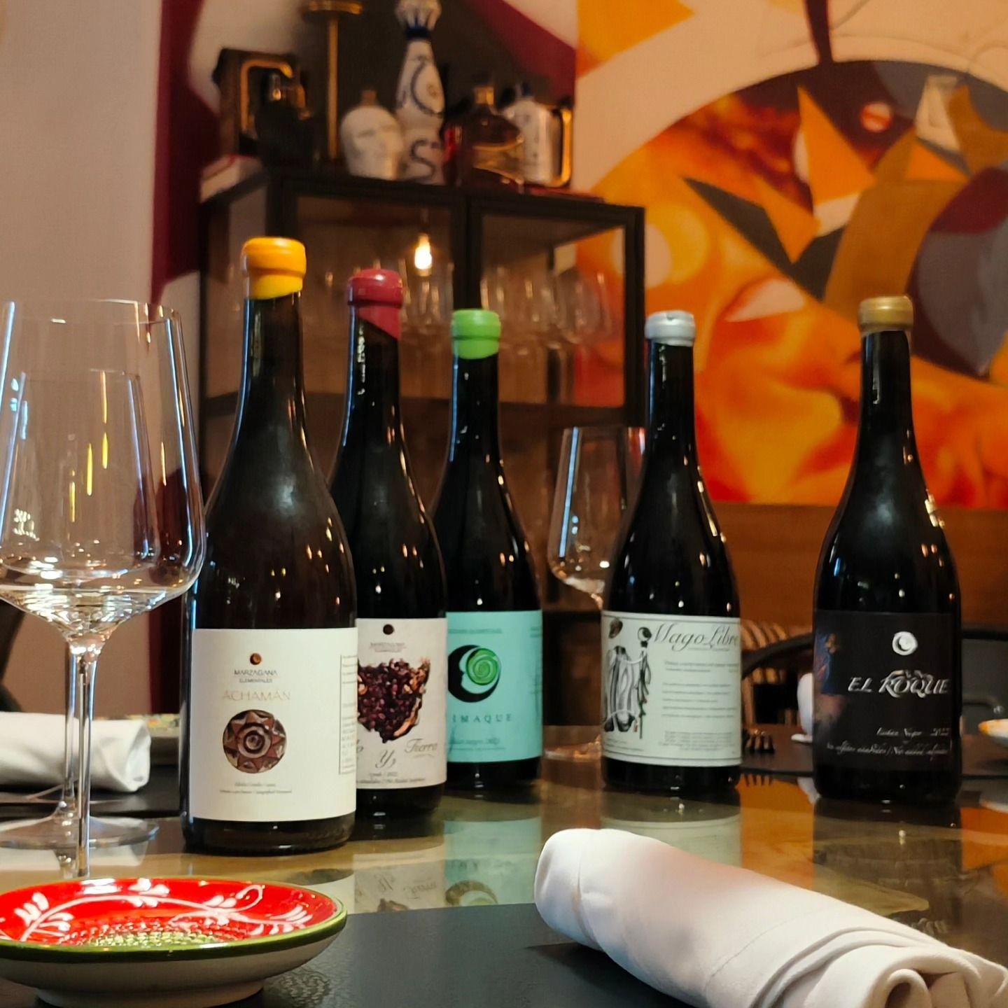 Hay varias botellas de vino sobre una mesa, incluida una llamada El Rojo.