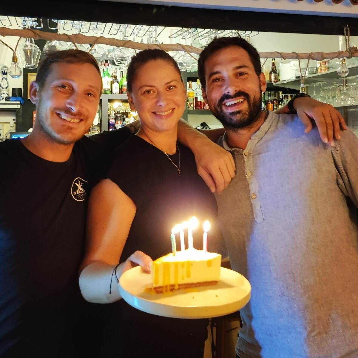 Dos hombres y una mujer sosteniendo un pastel con velas.