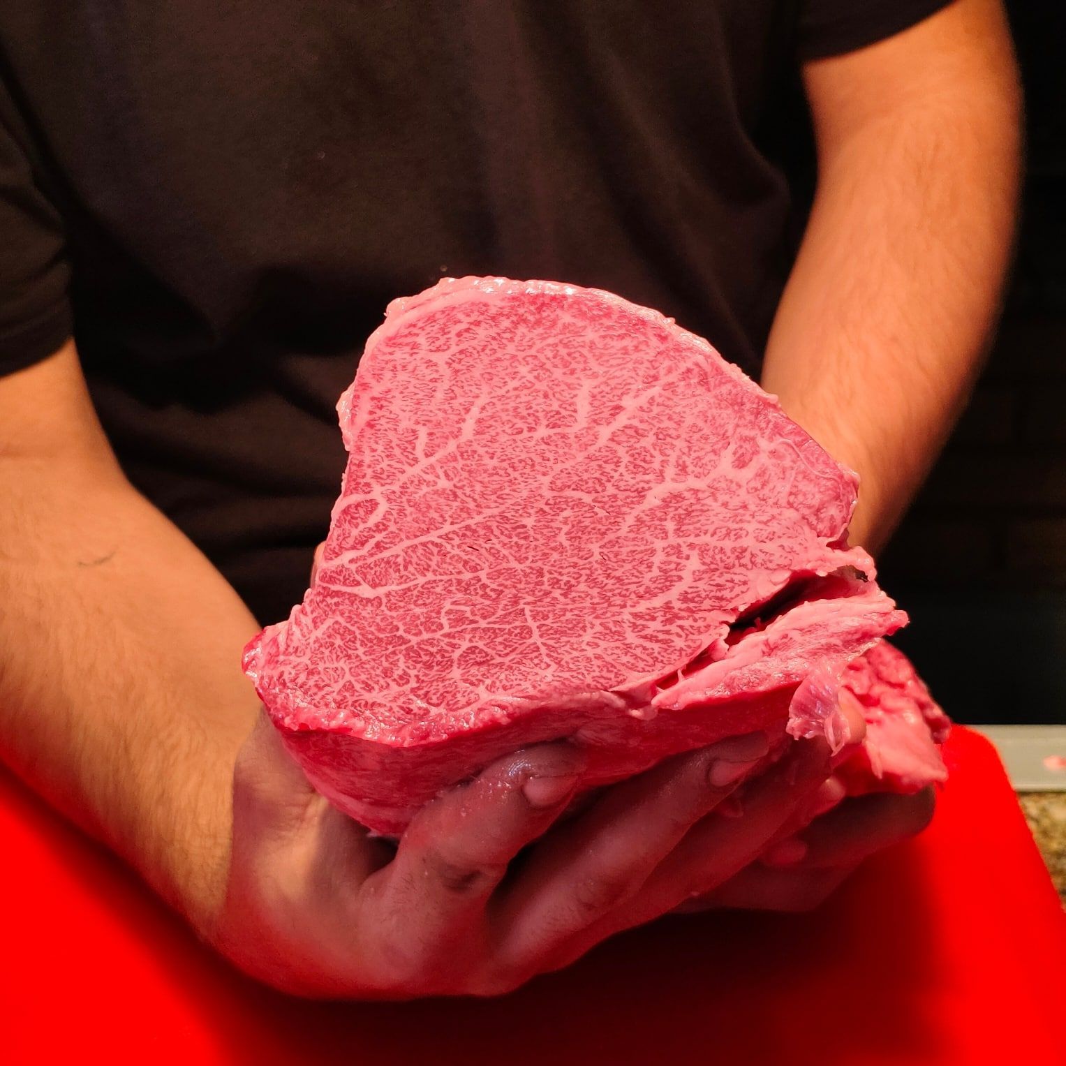 Una persona sostiene un trozo de carne rosada en sus manos.