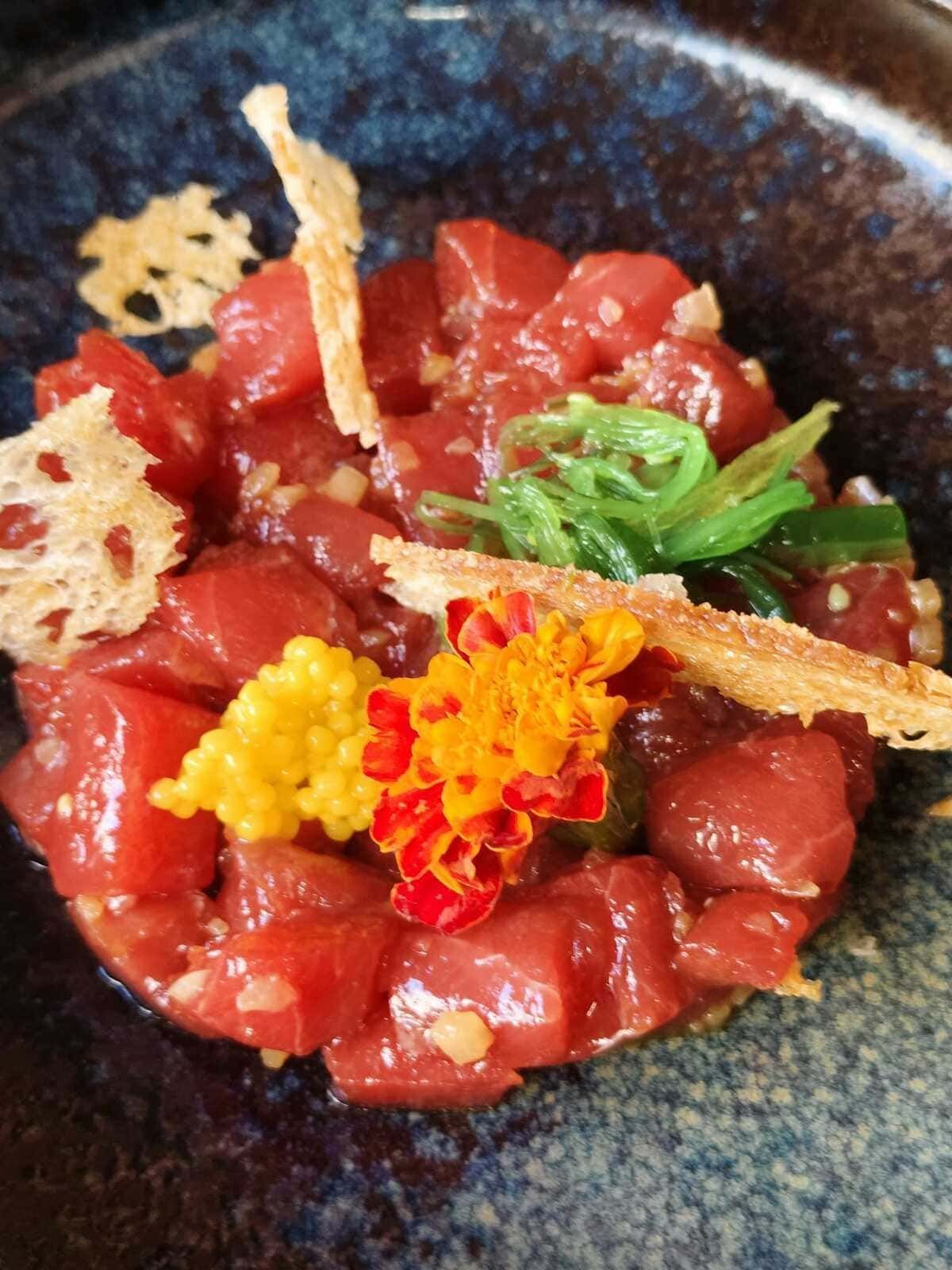 Sashimi de atún crudo dispuesto en un bol con hierbas aromáticas y una colorida guarnición.