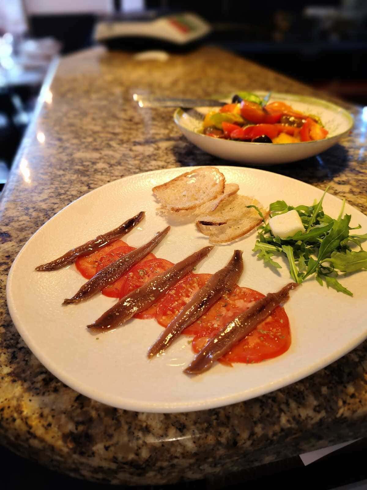 Filete en rodajas servido en un plato con pan y verduras sobre una encimera, con un tazón de verduras detrás.