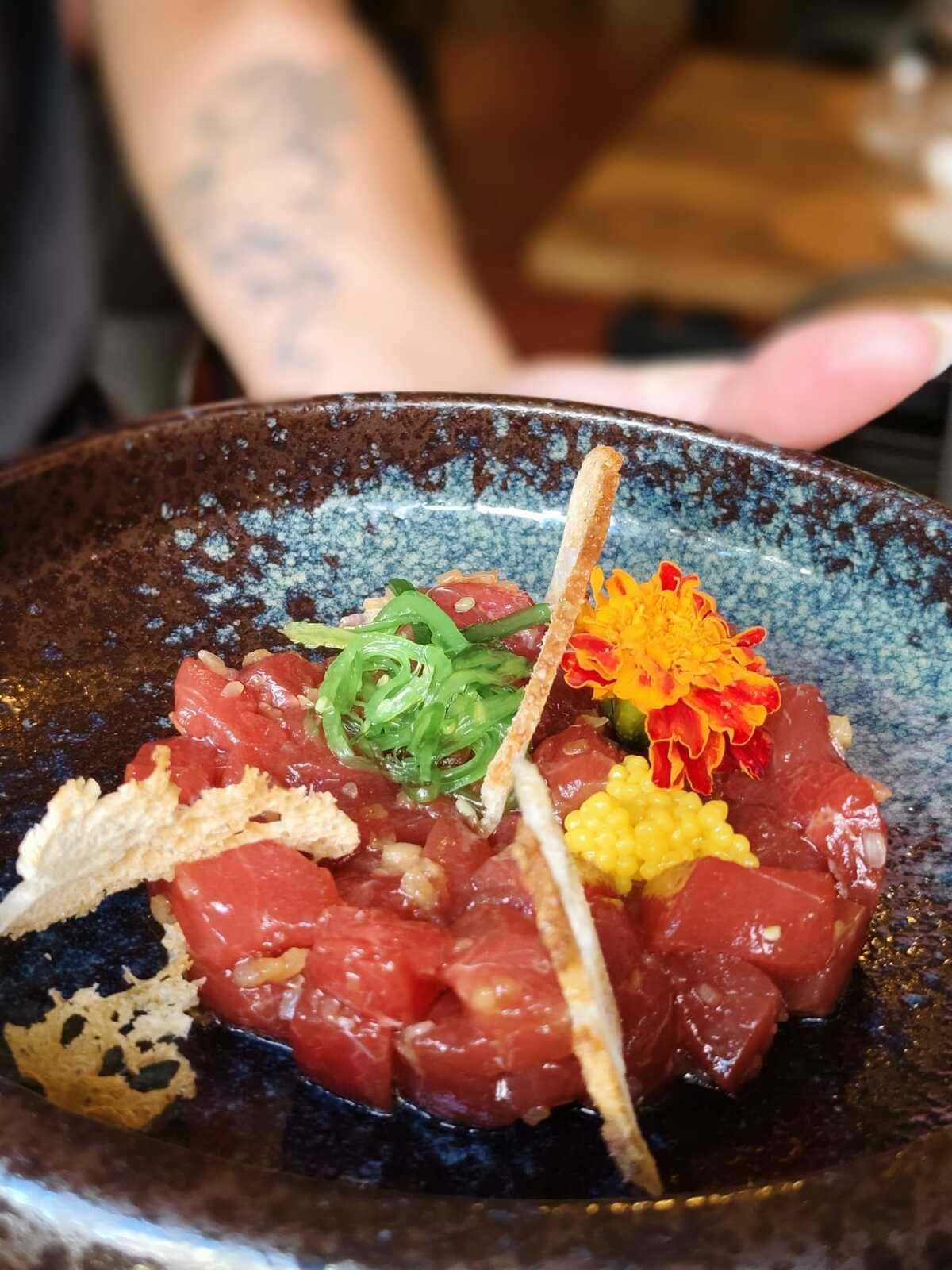 Tartar de atún en un bol rústico, cubierto con cebolleta, mostaza y guarnición crujiente.