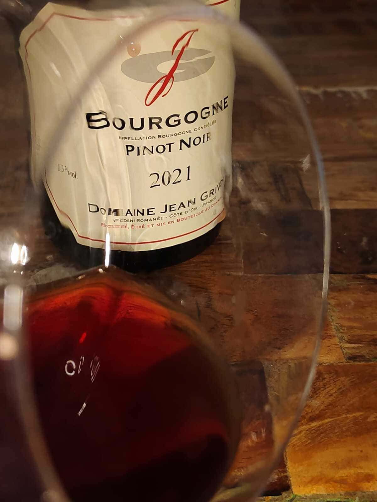 Una copa de vino tinto frente a una botella de Bourgogne Pinot Noir 2021 sobre una mesa de madera.