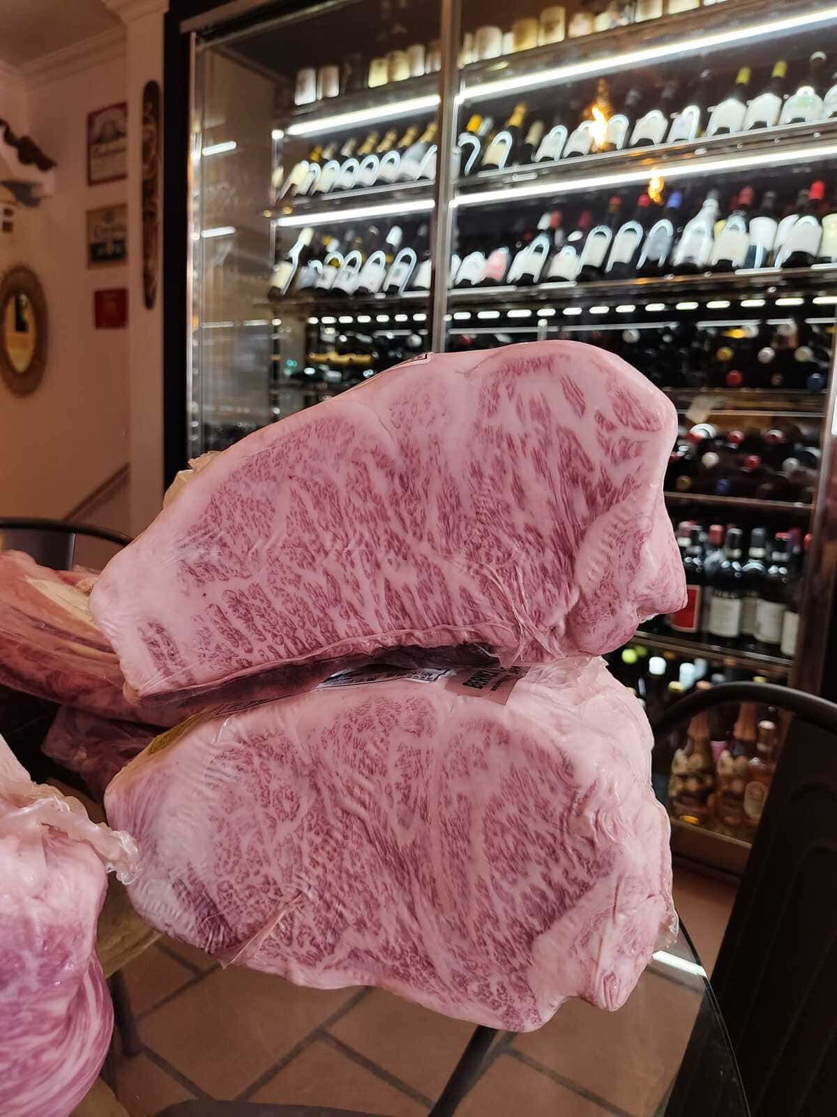 Dos gruesos filetes de ternera veteada expuestos frente a una pared de vinos.