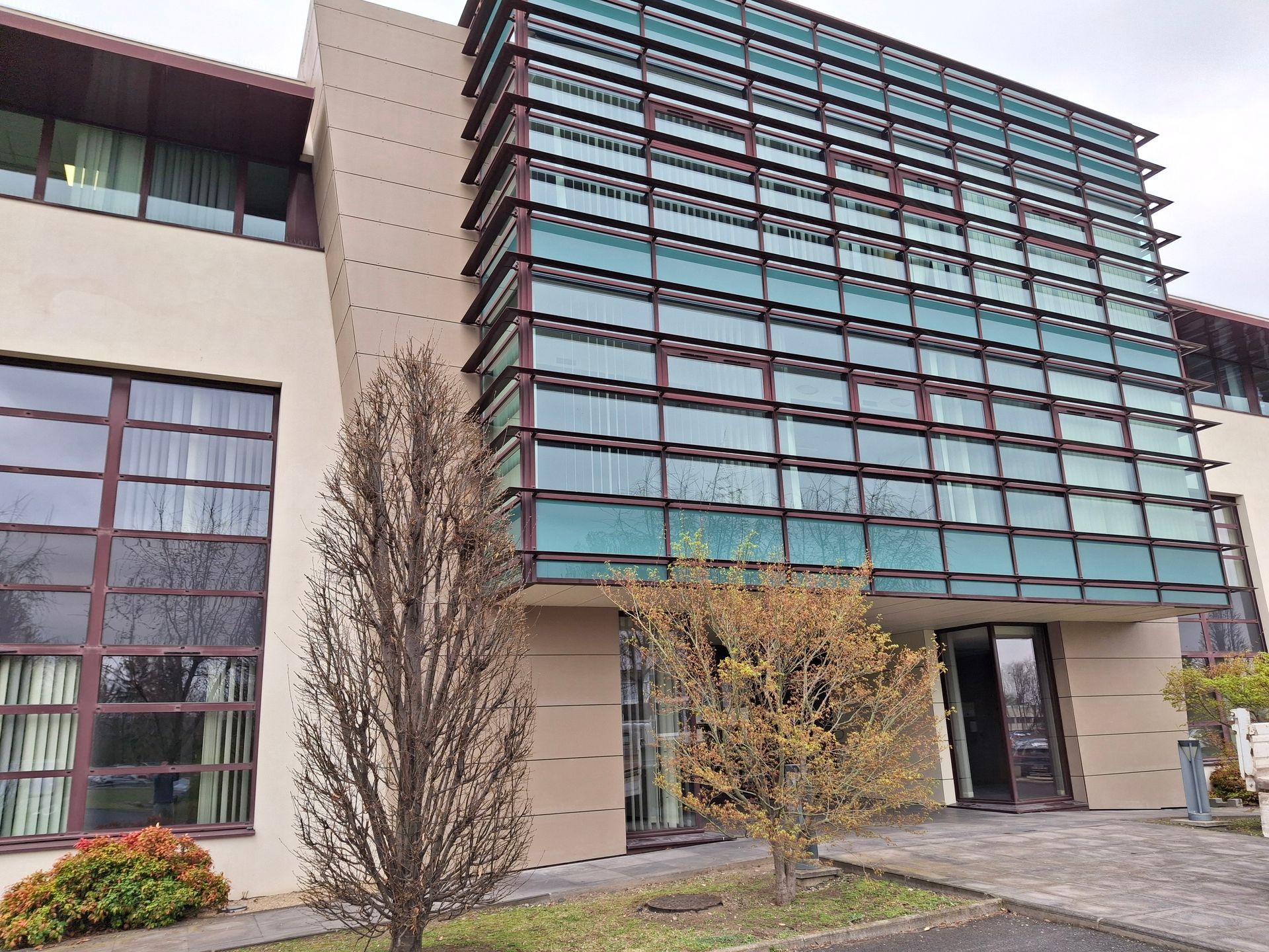 Bâtiment moderne avec façade en verre et couleur beige, arbres devant.
