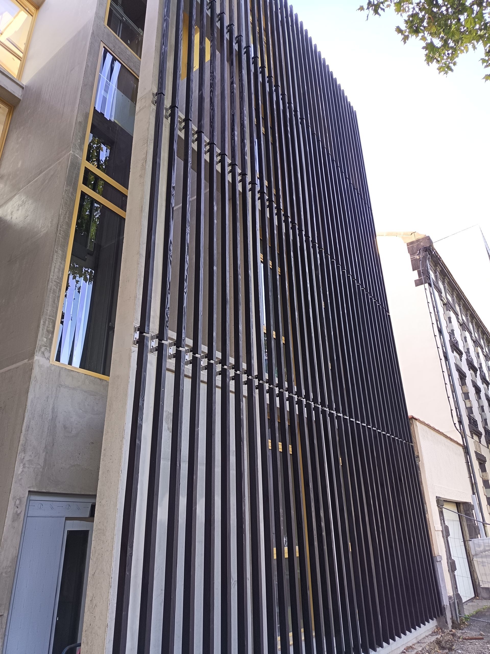 Bâtiment moderne dont la façade est recouverte de lattes verticales noires, avec des fenêtres et une porte.