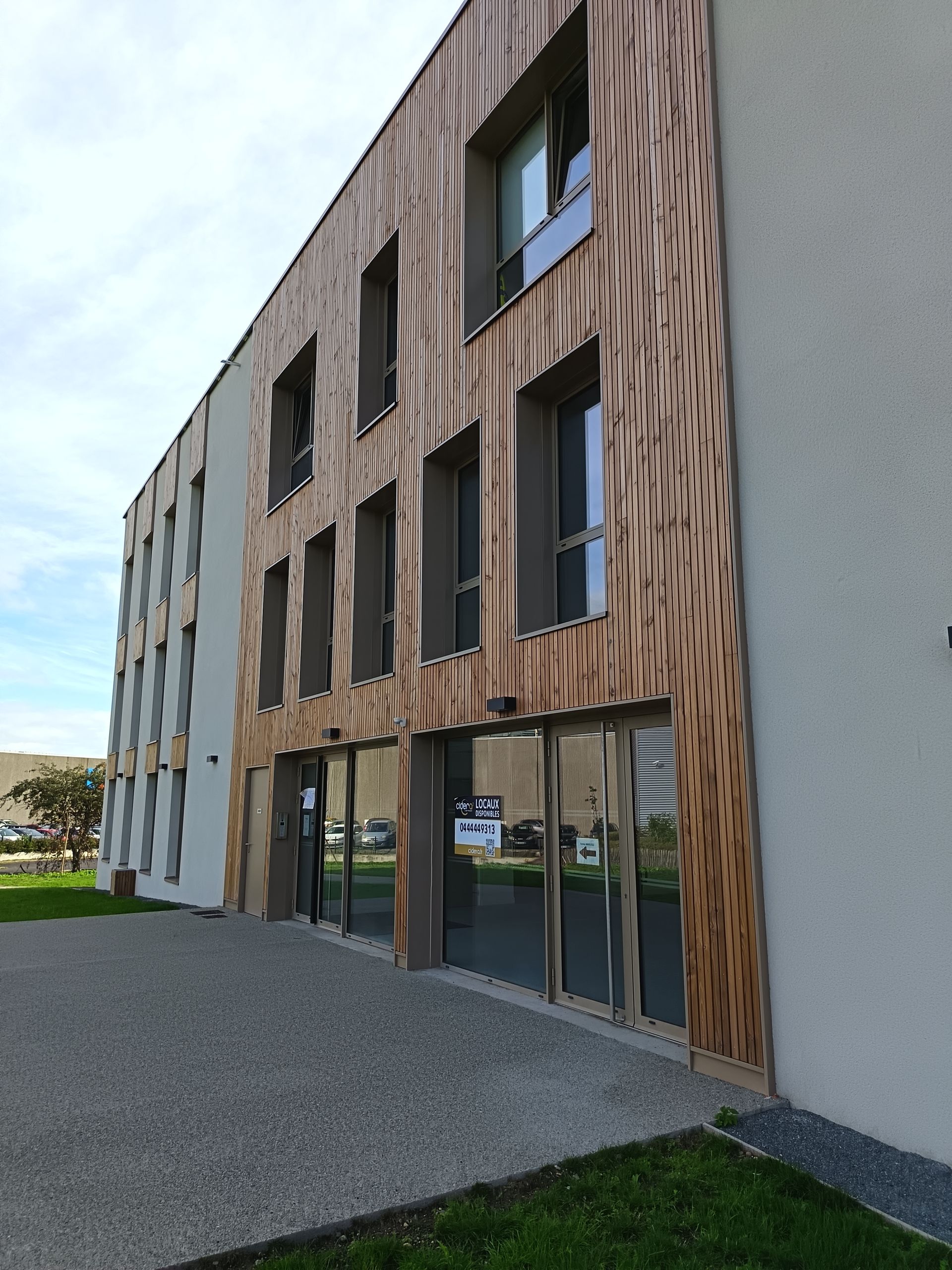 Bâtiment moderne avec façade en bois, fenêtres et portes vitrées. Terrasse en pierre grise.