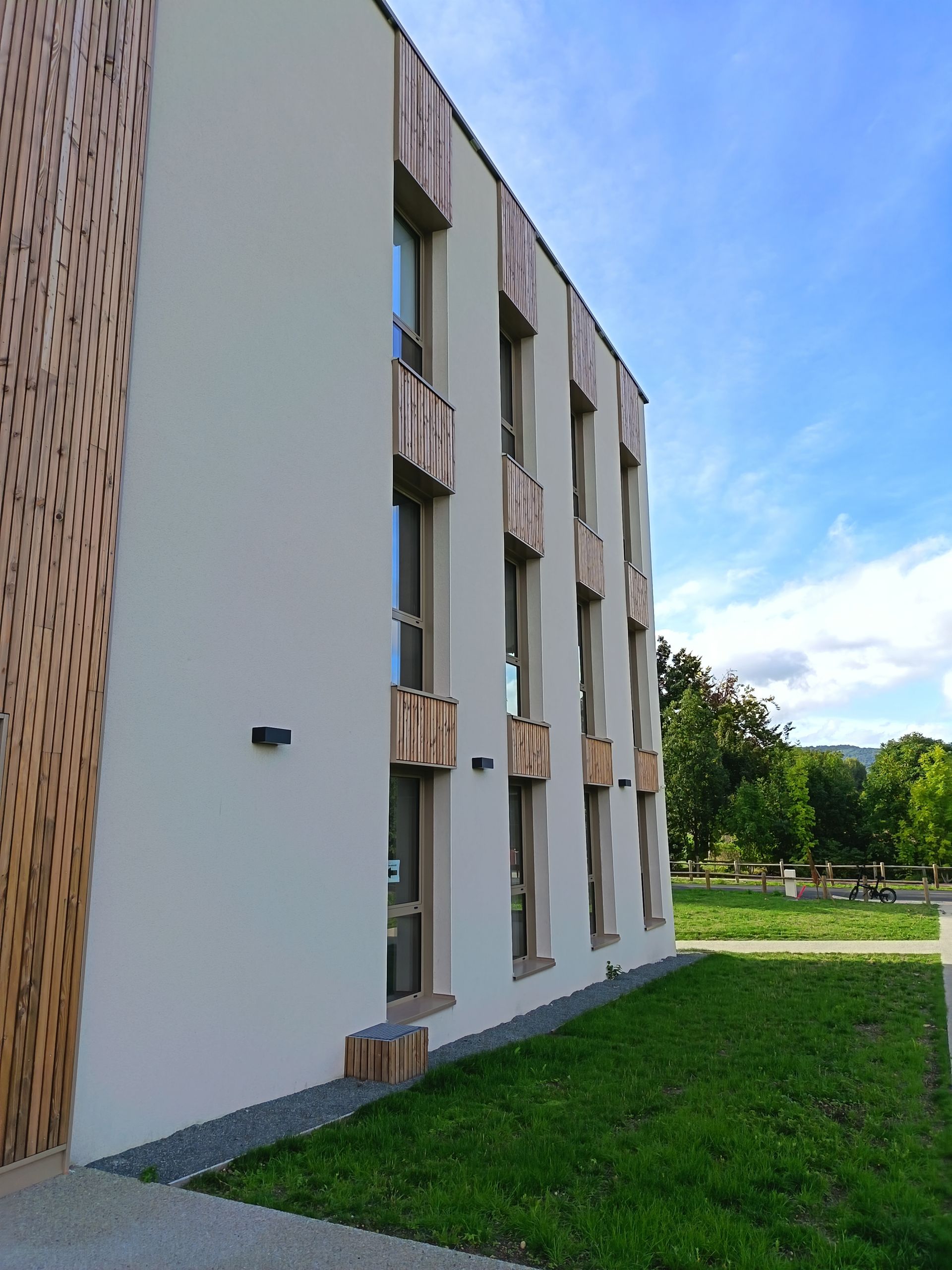 Extérieur d'un bâtiment moderne avec des éléments en bois par une journée ensoleillée.