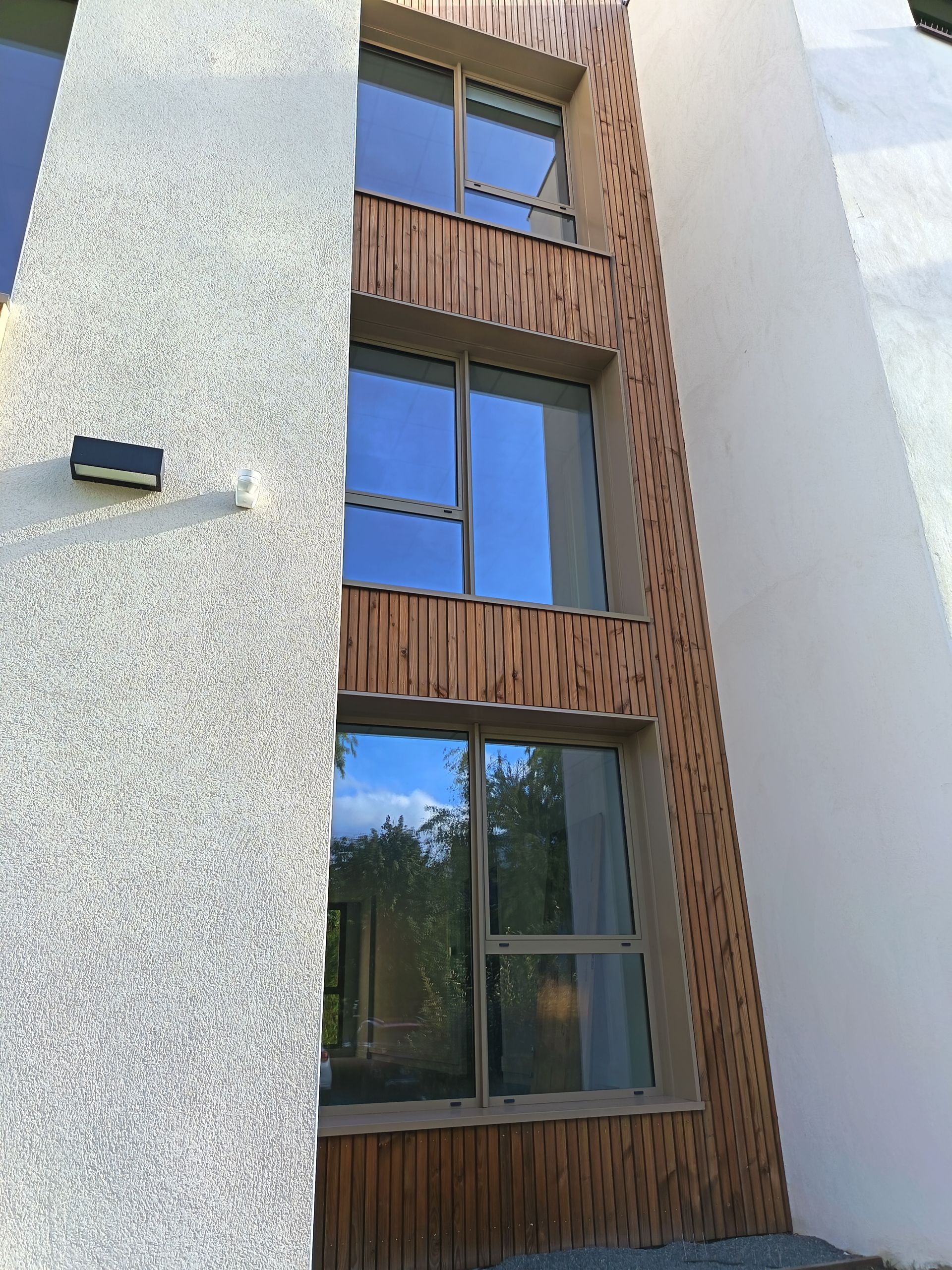 Extérieur d'un bâtiment avec une enseigne de traiteur ; lambris en bois beige et foncé, fenêtres et parking.