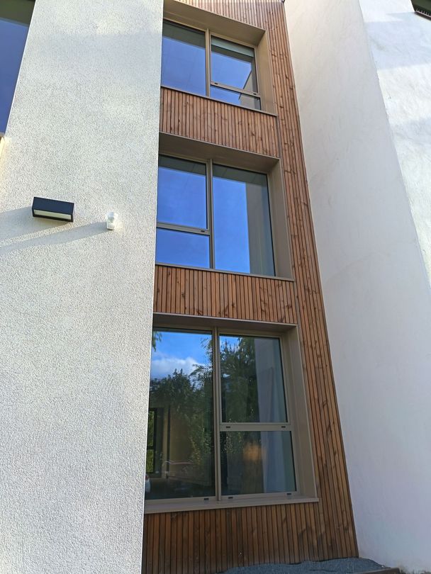 Extérieur d'un bâtiment avec une enseigne de traiteur ; lambris en bois beige et foncé, fenêtres et parking.