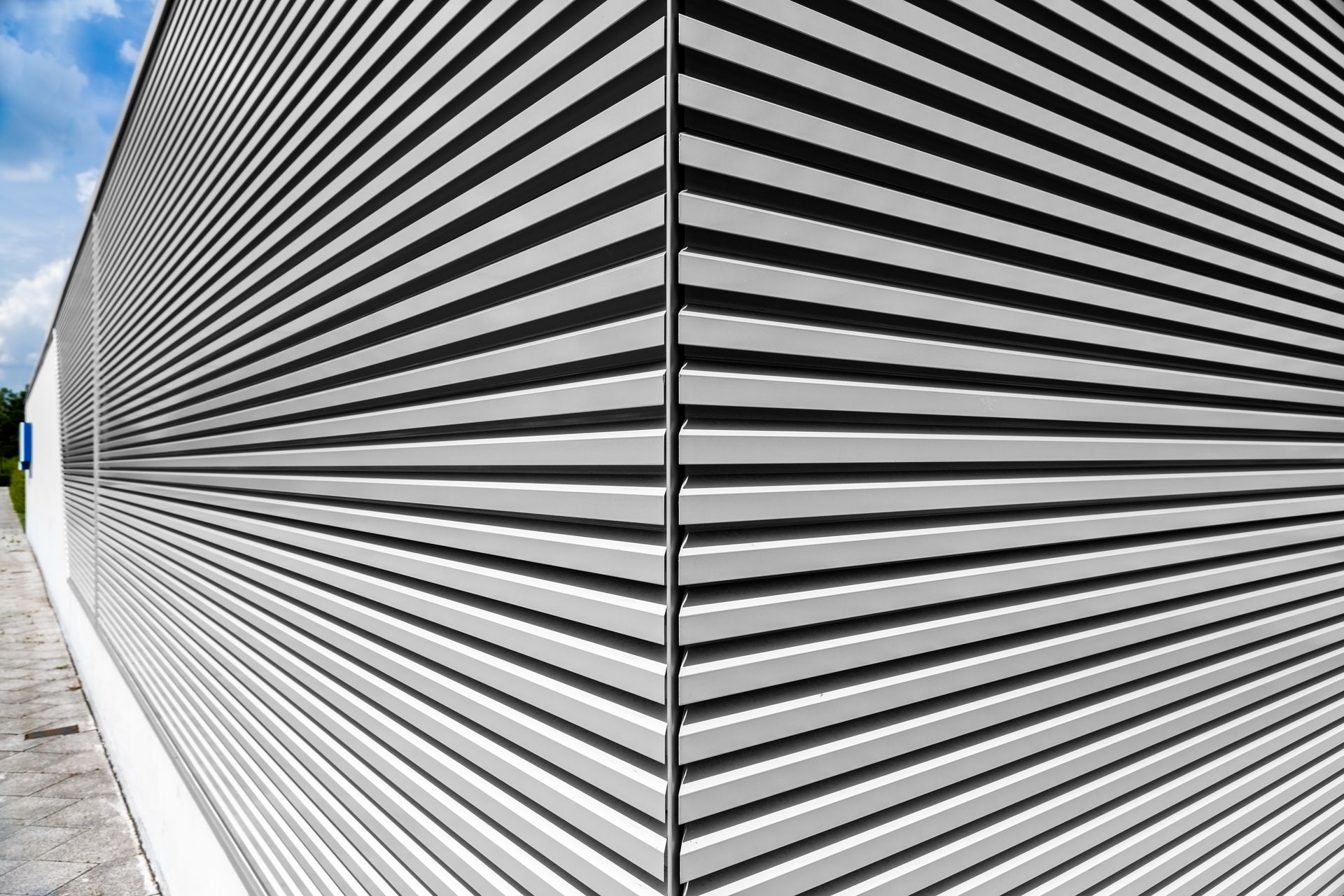 Angle d'un bâtiment en métal gris à nervures horizontales se détachant sur un ciel nuageux.