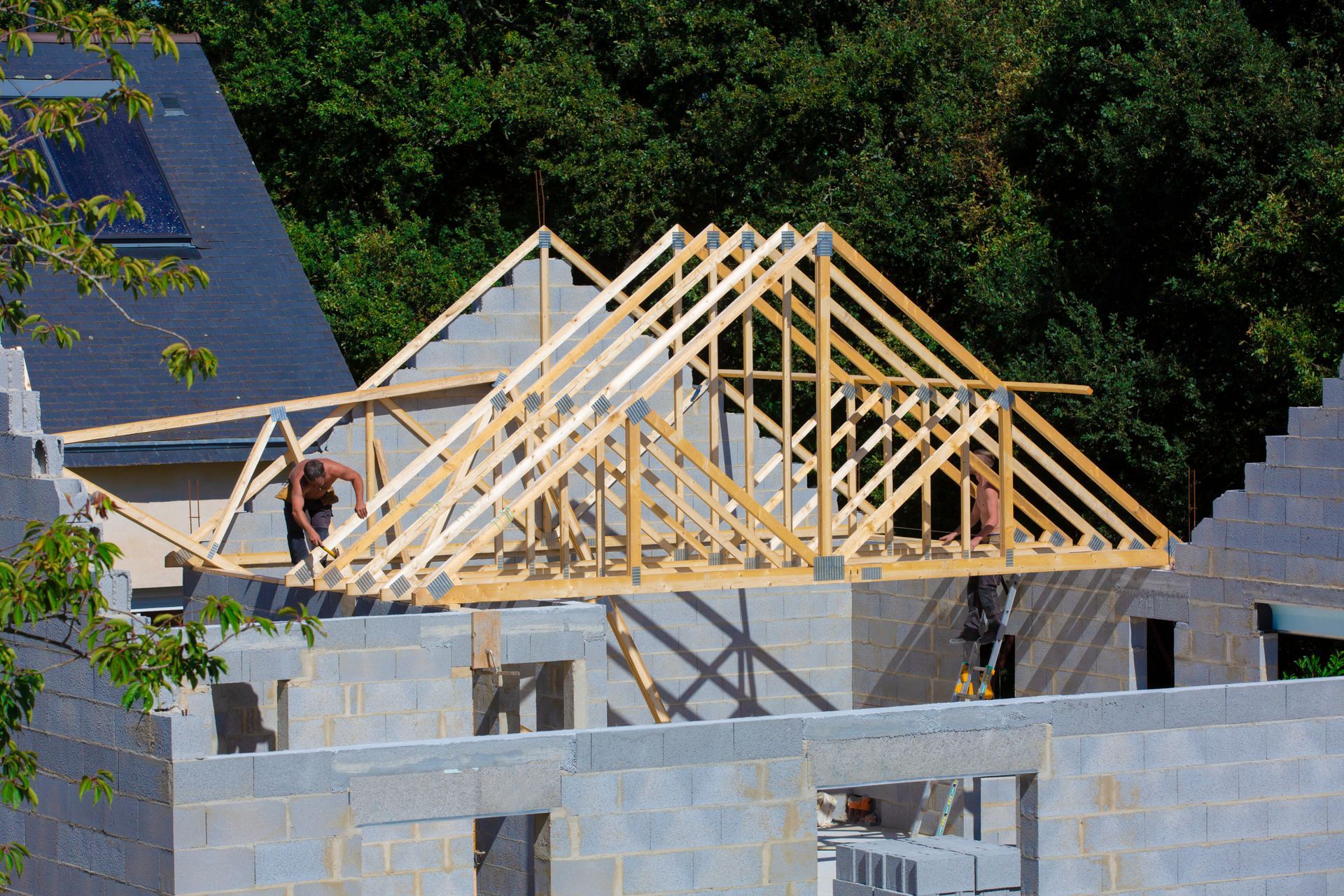 Construction d'une charpente de toit. Des fermes en bois sont installées sur un bâtiment en parpaings gris par des ouvriers du bâtiment.