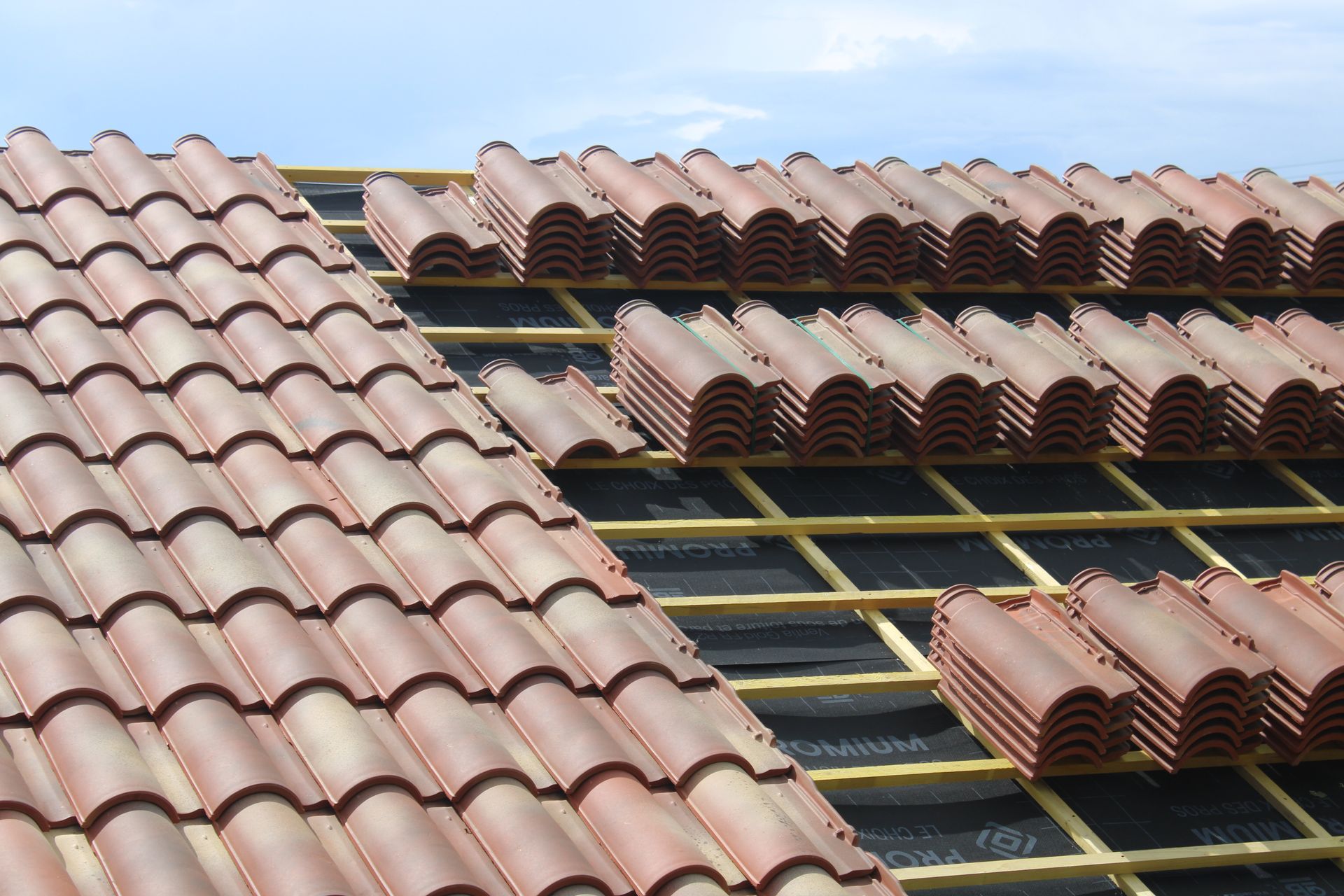 Toiture en cours de réalisation : pose de tuiles en terre cuite sur une charpente en bois.
